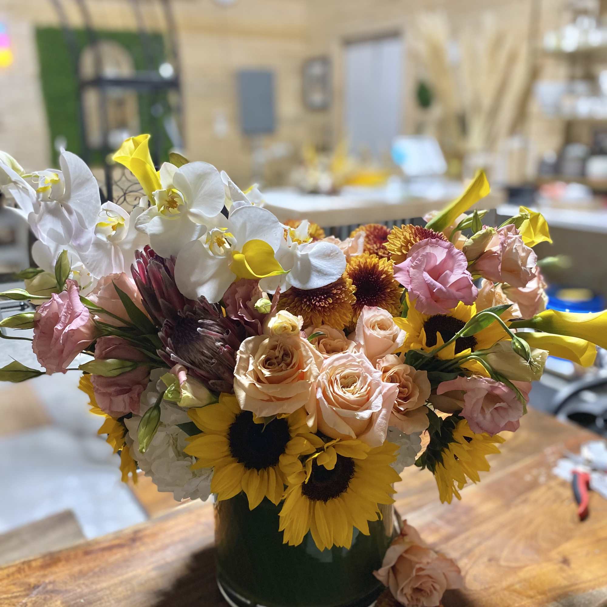 Mixed bouquet with white orchids, peach roses, sunflowers, and pink blooms in a dark vase
