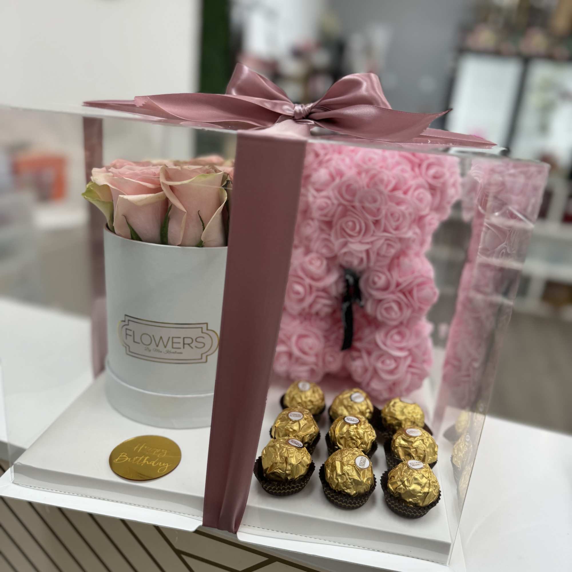 Pink roses in a gift box with gold-wrapped chocolates and a ribbon bow