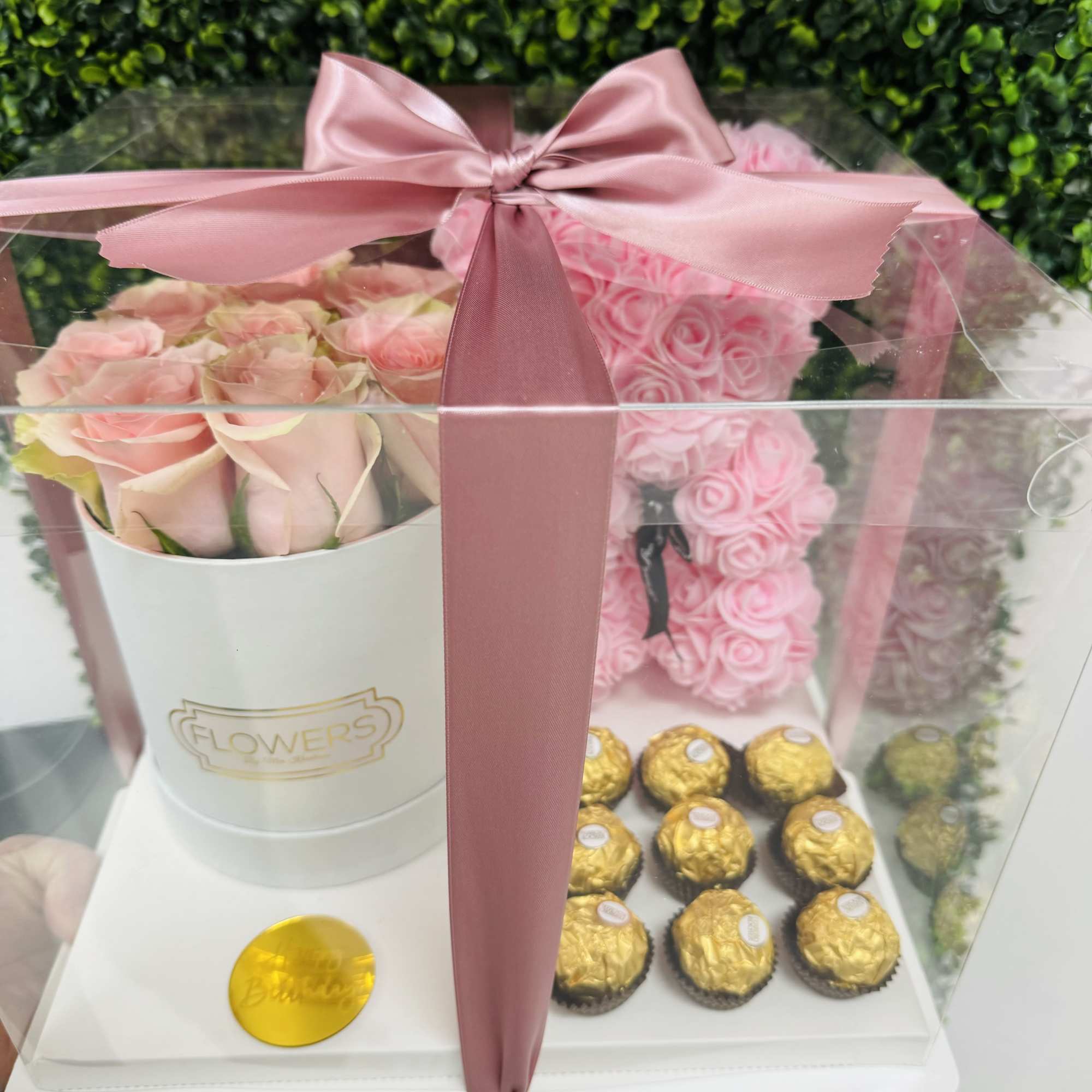Pink roses in a clear gift box with chocolates and a satin bow