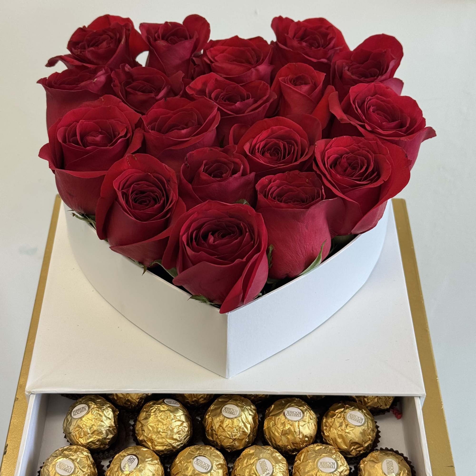 Red roses in a heart-shaped box above gold-wrapped chocolates