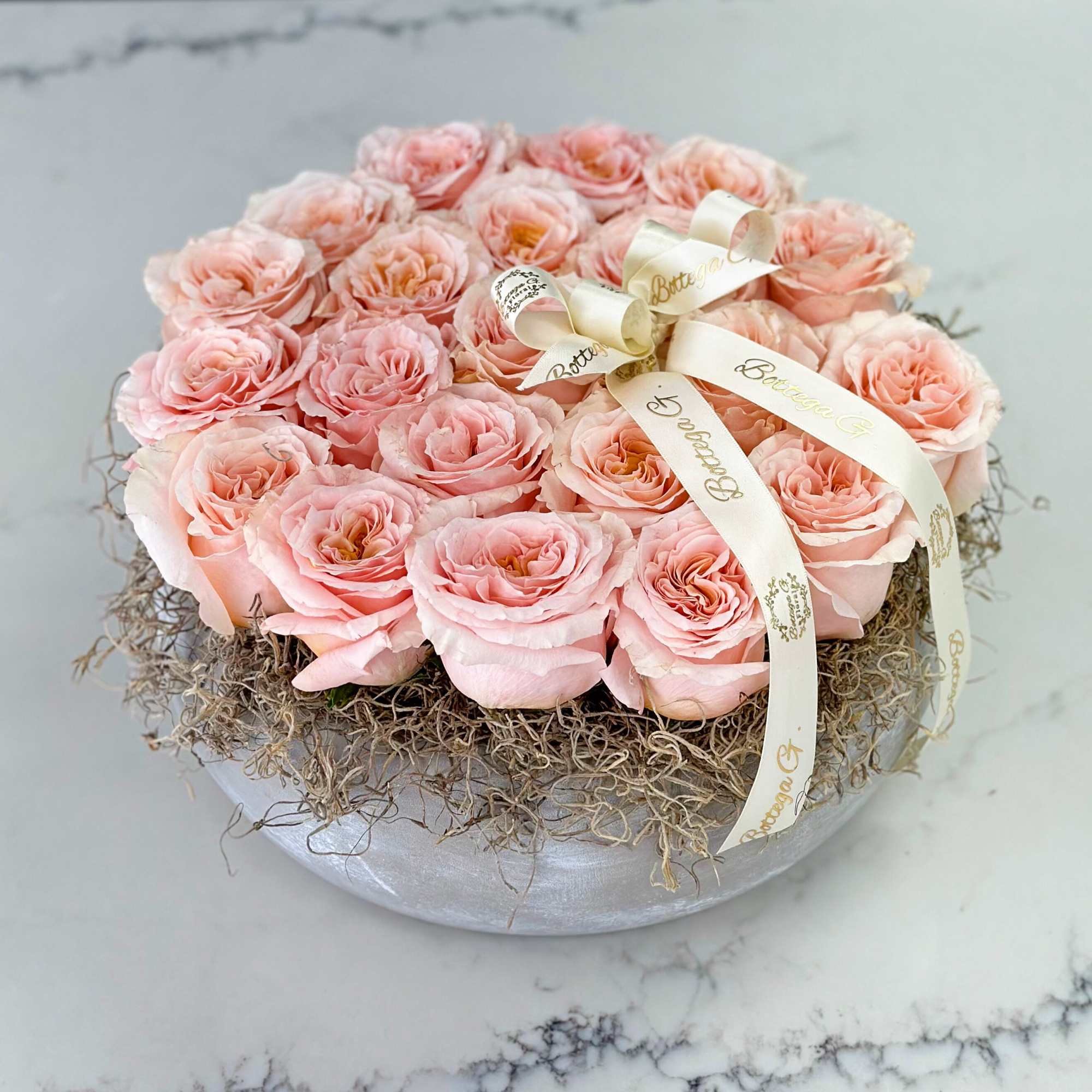 Round box of pale pink roses with a cream ribbon