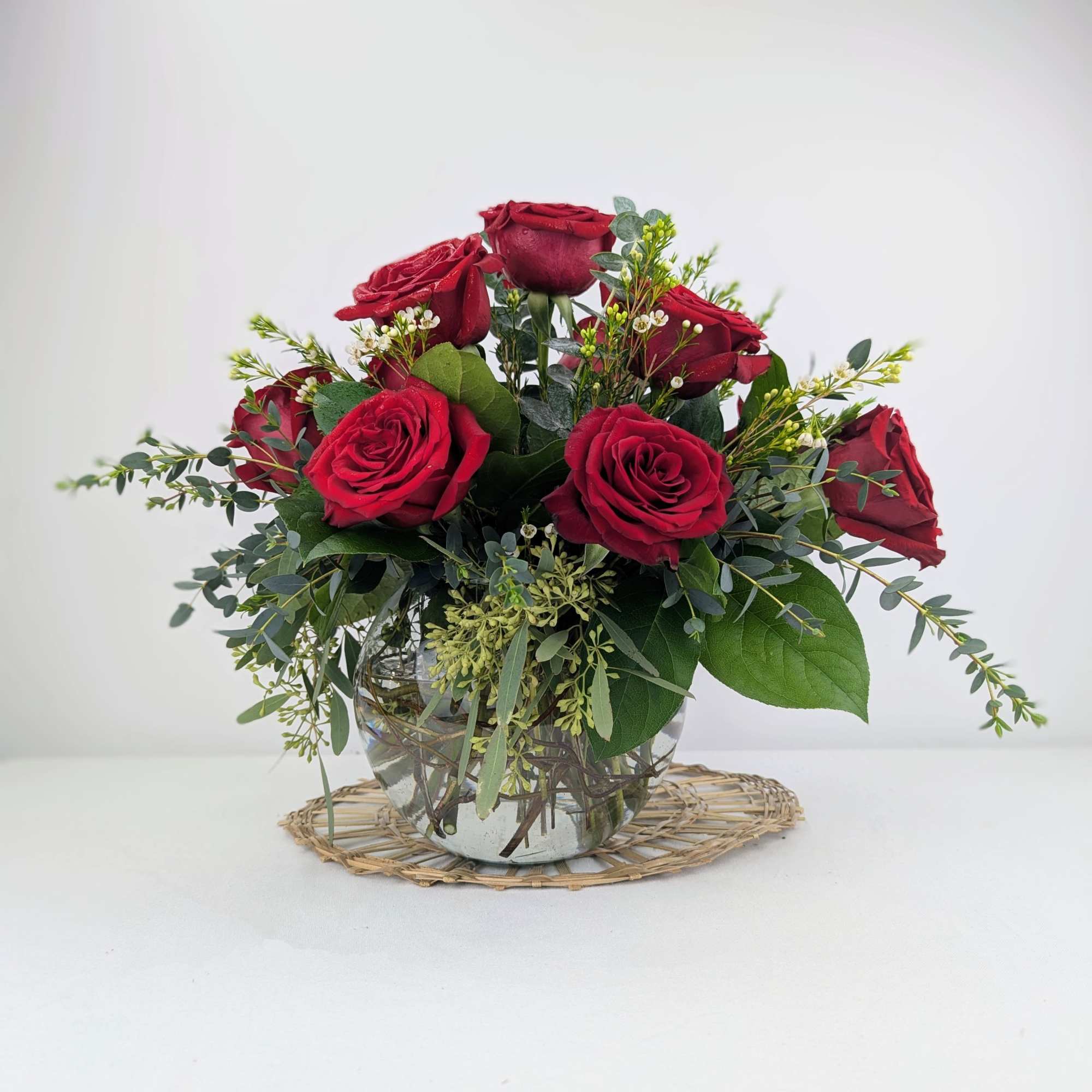 Red roses arranged in a clear glass vase with greenery