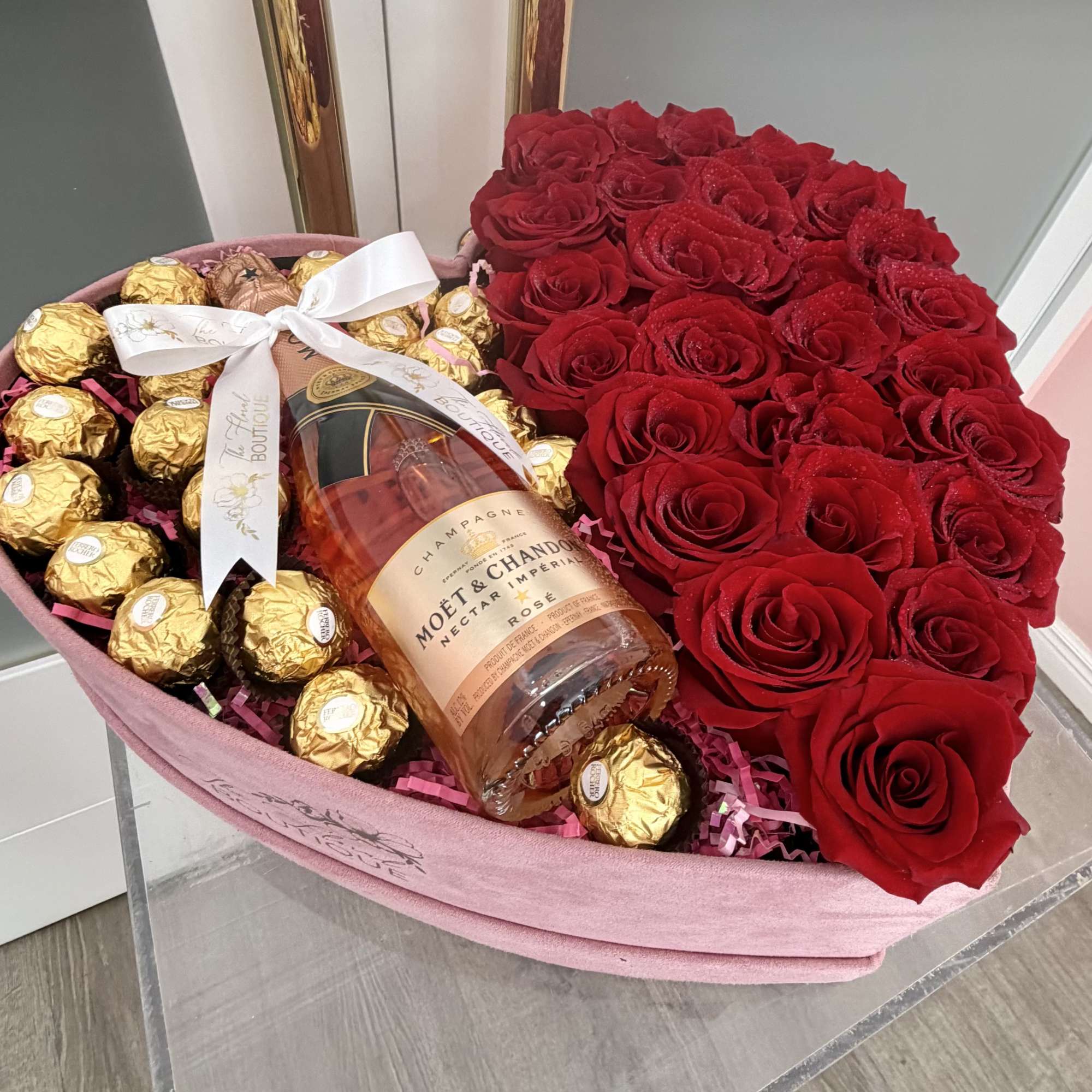 Heart-shaped box of red roses with chocolates and a champagne bottle