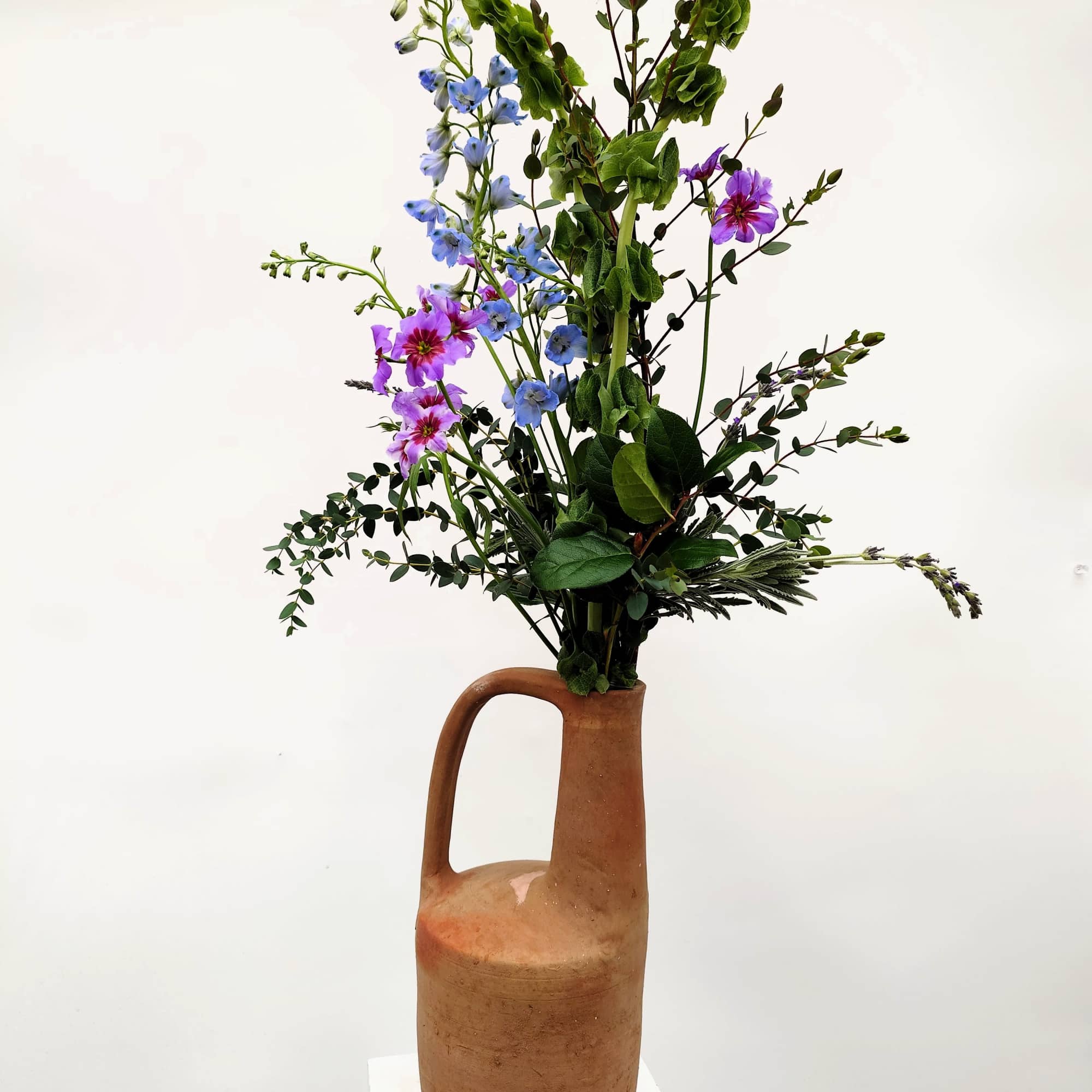 A sculptural floral arrangement designed in a tall, long-necked clay pitcher, Juno