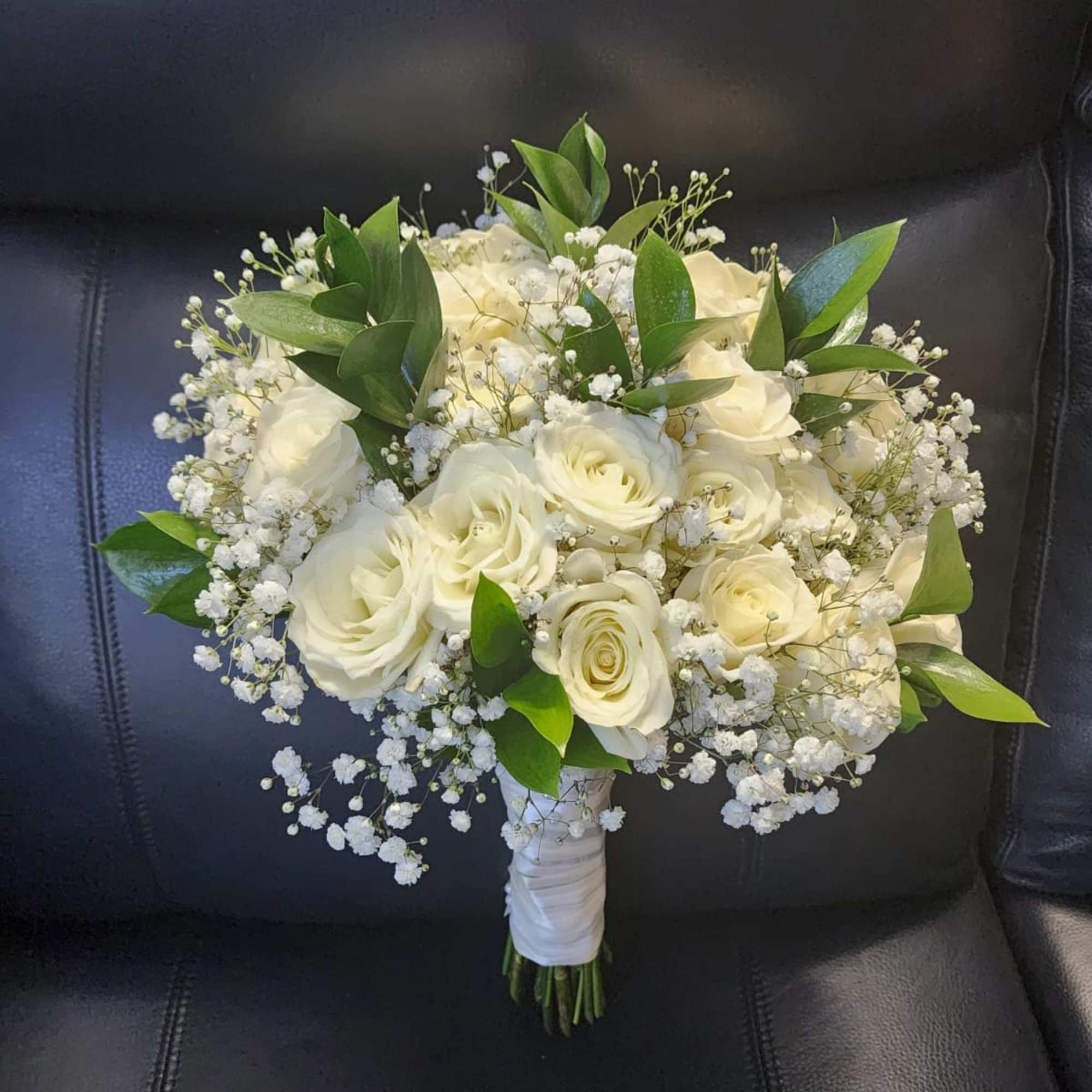 White roses complemented by delicate baby&rsquo;s breath and lush greenery. Wrapped with