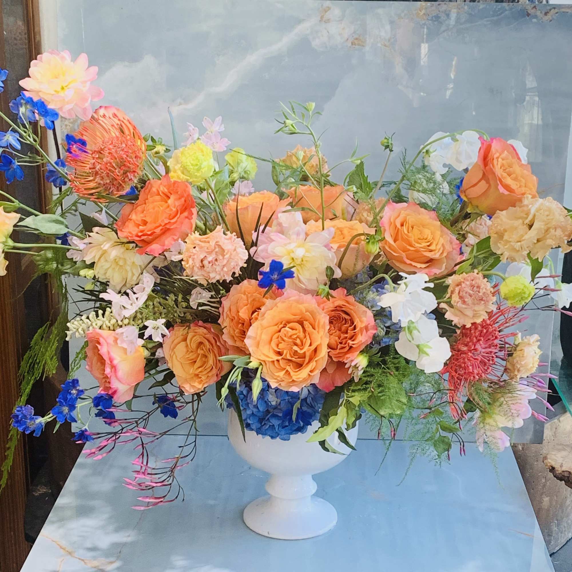 This arrangement feels bright, garden-inspired, and joyful, with the coral and peach