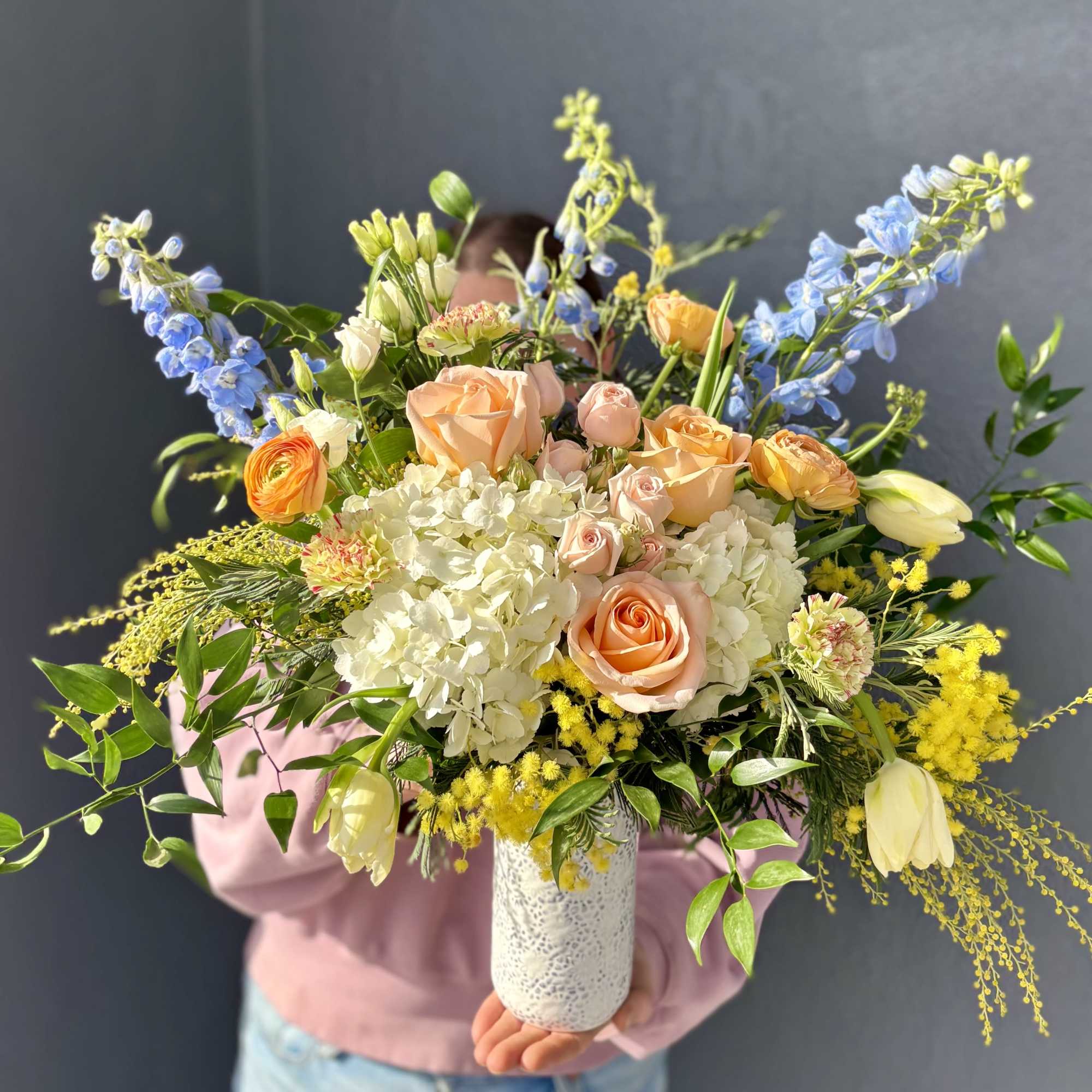 A bright and cheery seasonal arrangement. Vibrant and fragrant Mimosa compliment calming