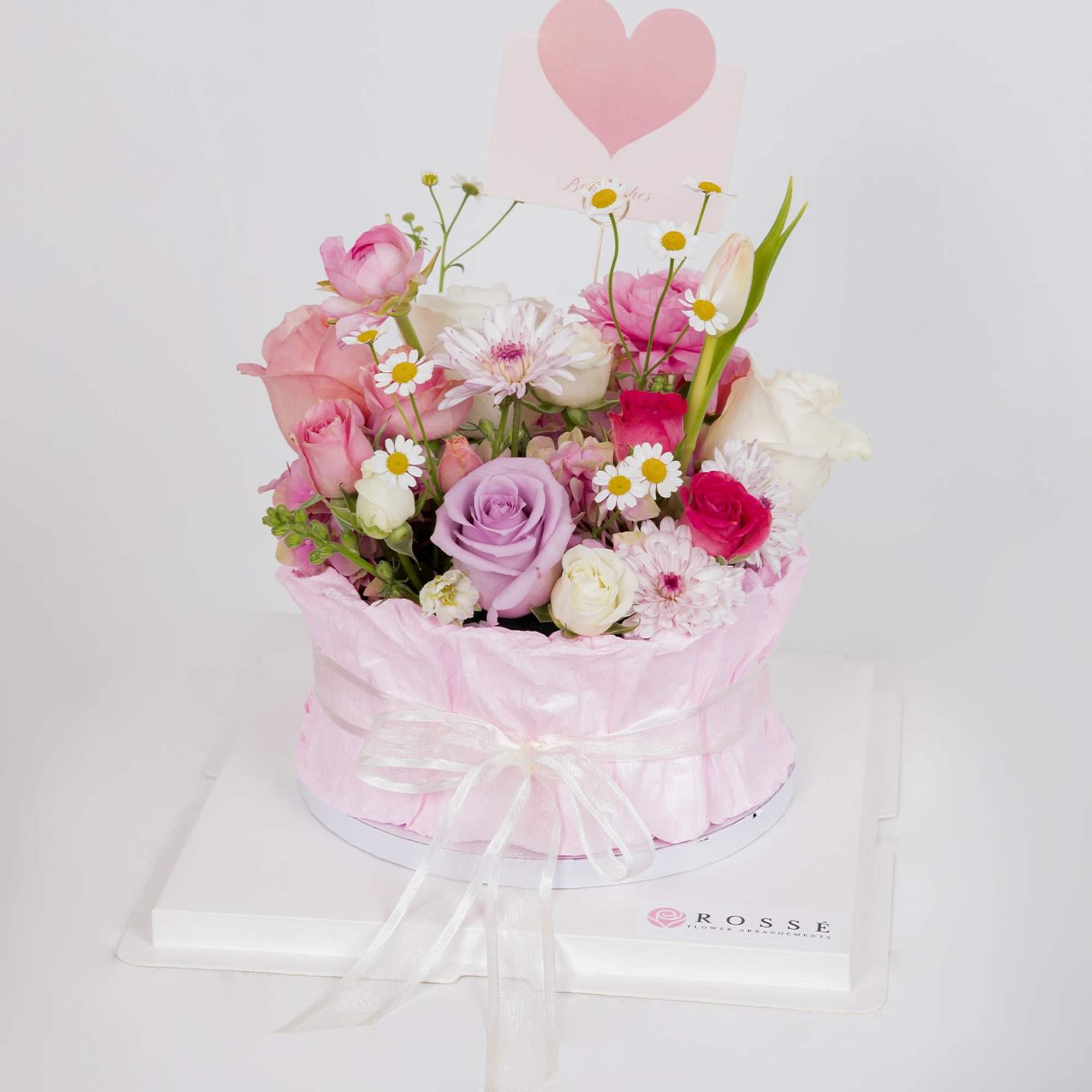A cake-inspired floral design featuring roses and seasonal blooms in soft pink