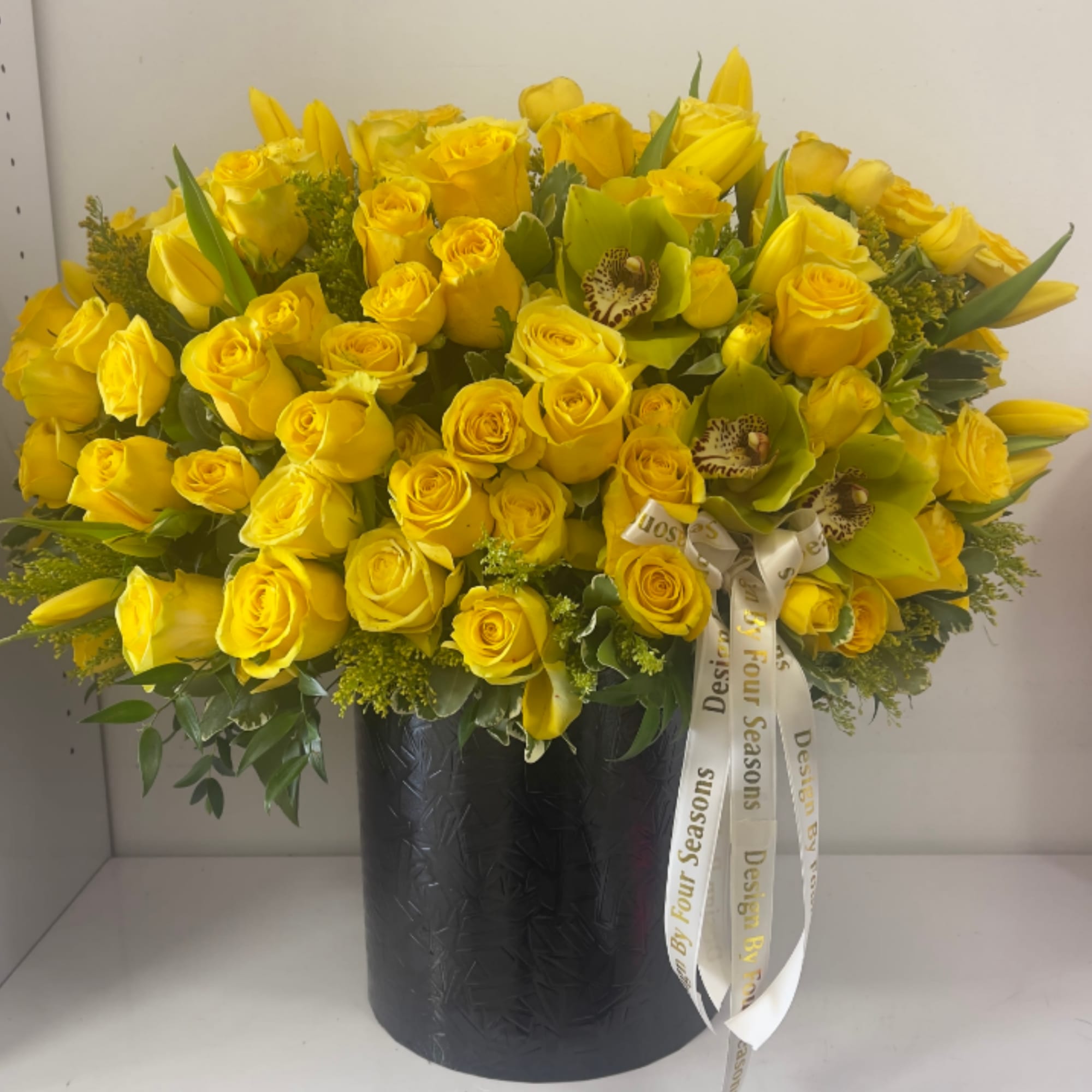 Yellow roses and tulips arranged in a black vase with a ribbon