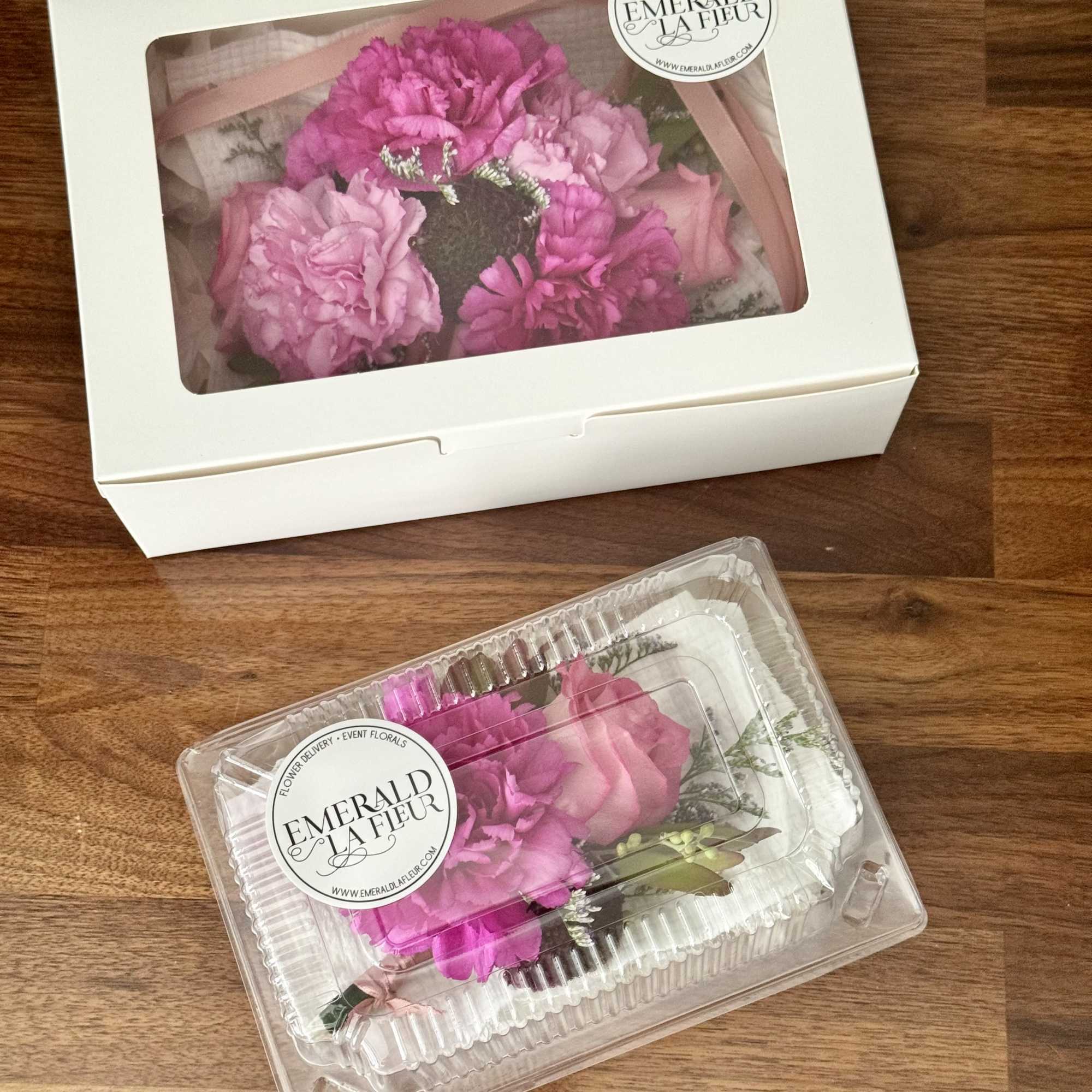 Two boxed pink floral arrangements on a wooden surface