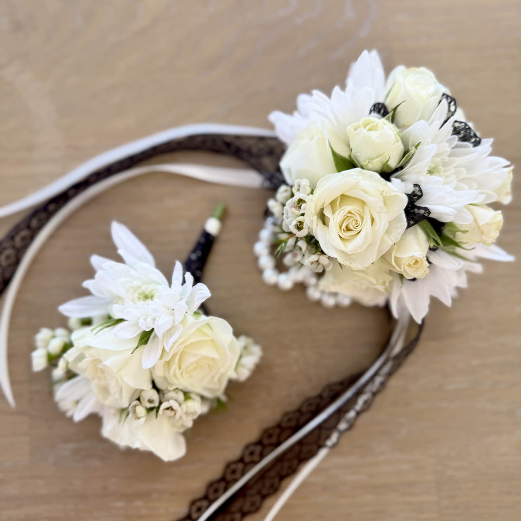 Two white floral wrist corsages with ribbon bands on a wooden surface