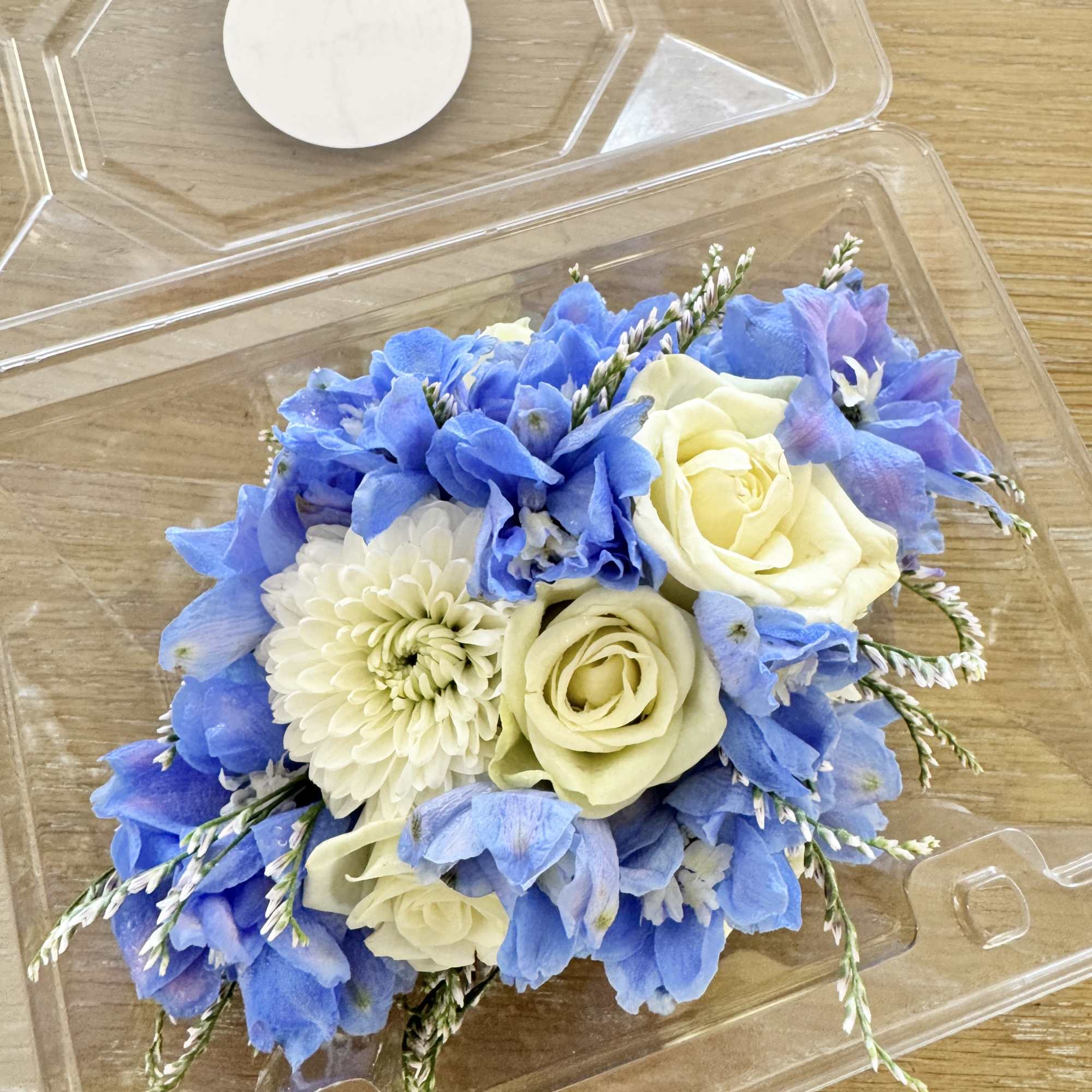 Blue and cream floral arrangement in a clear plastic box