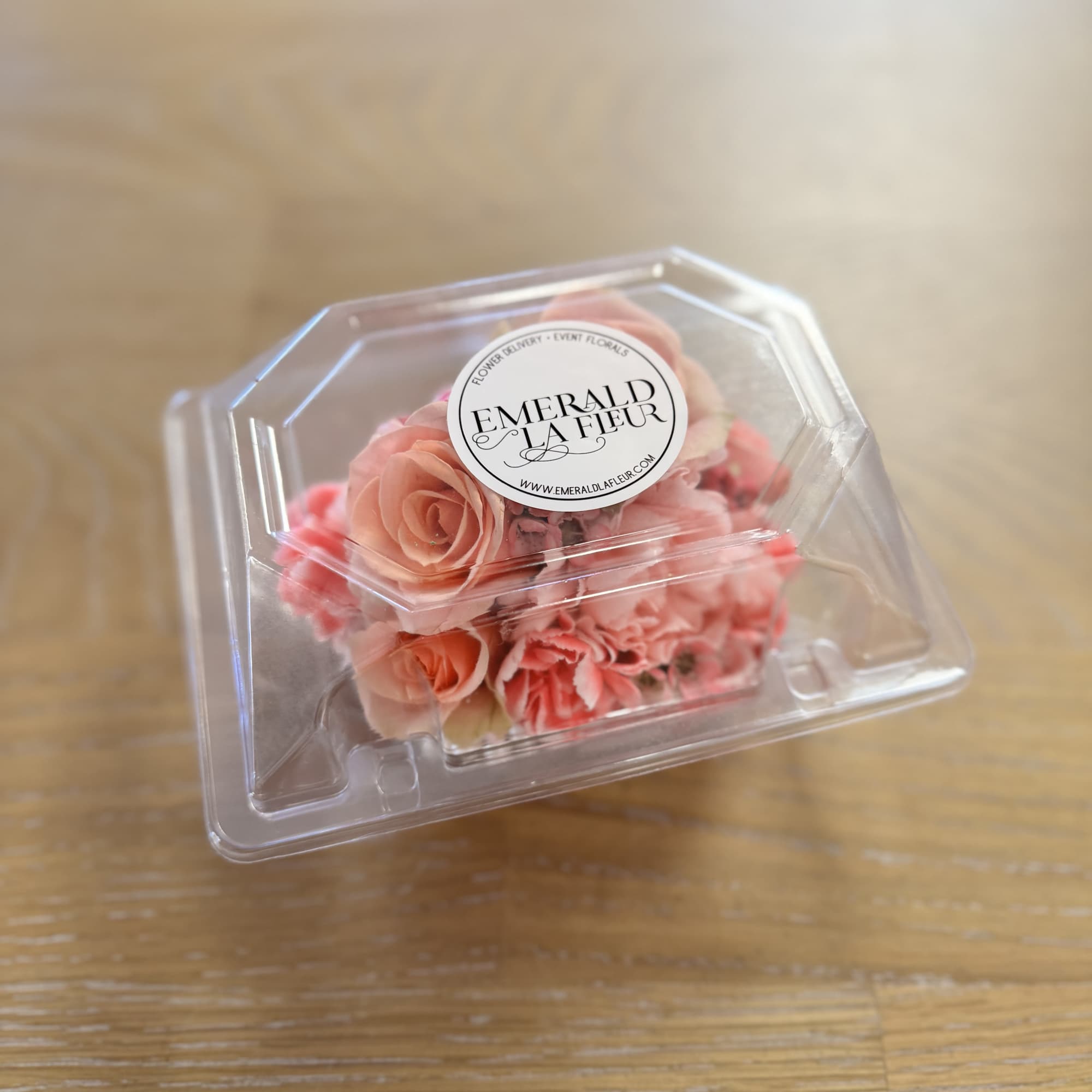 Small pink floral arrangement in a clear plastic box
