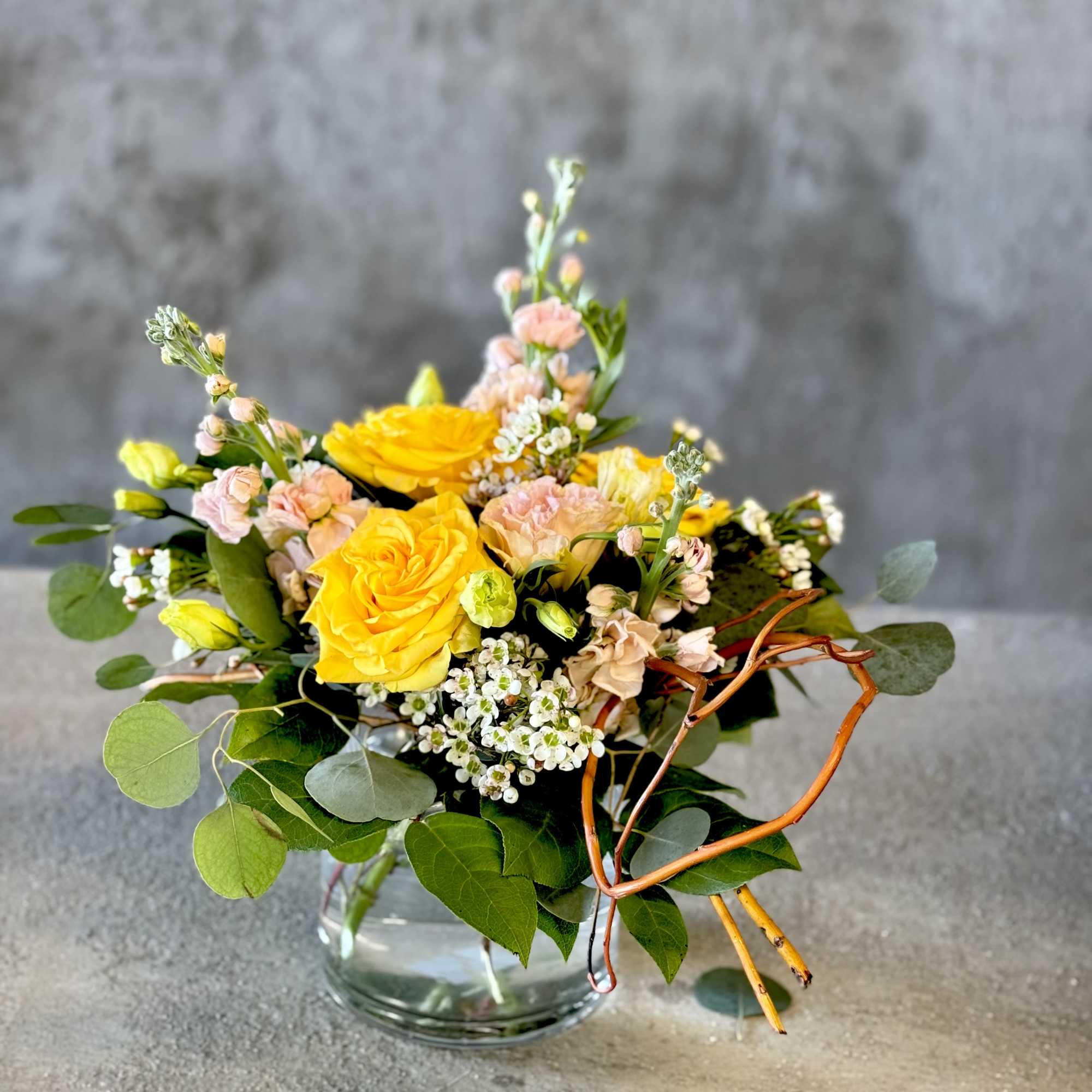 Yellow and blush roses in a clear glass vase with greenery