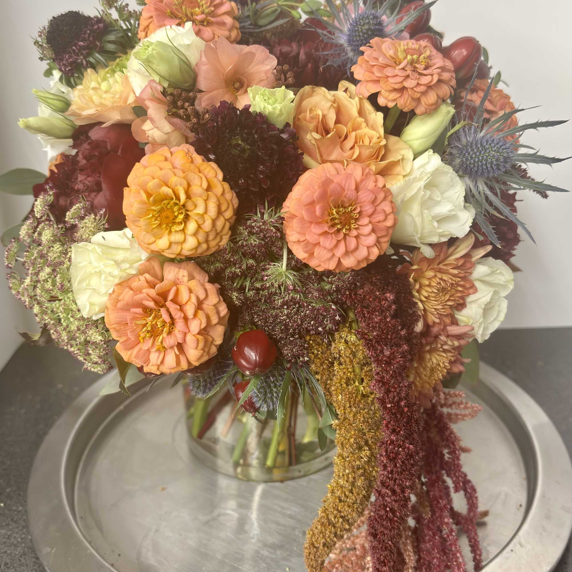 Mixed bouquet of orange, peach, white, and burgundy flowers in a glass vase