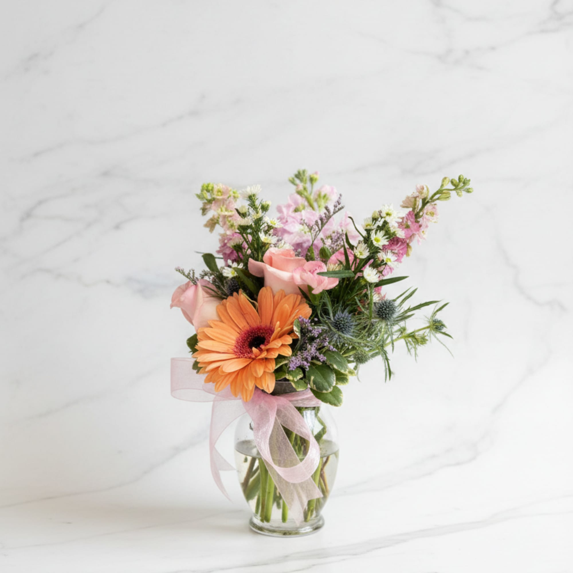 Pink and orange mixed bouquet in a clear glass vase with a ribbon