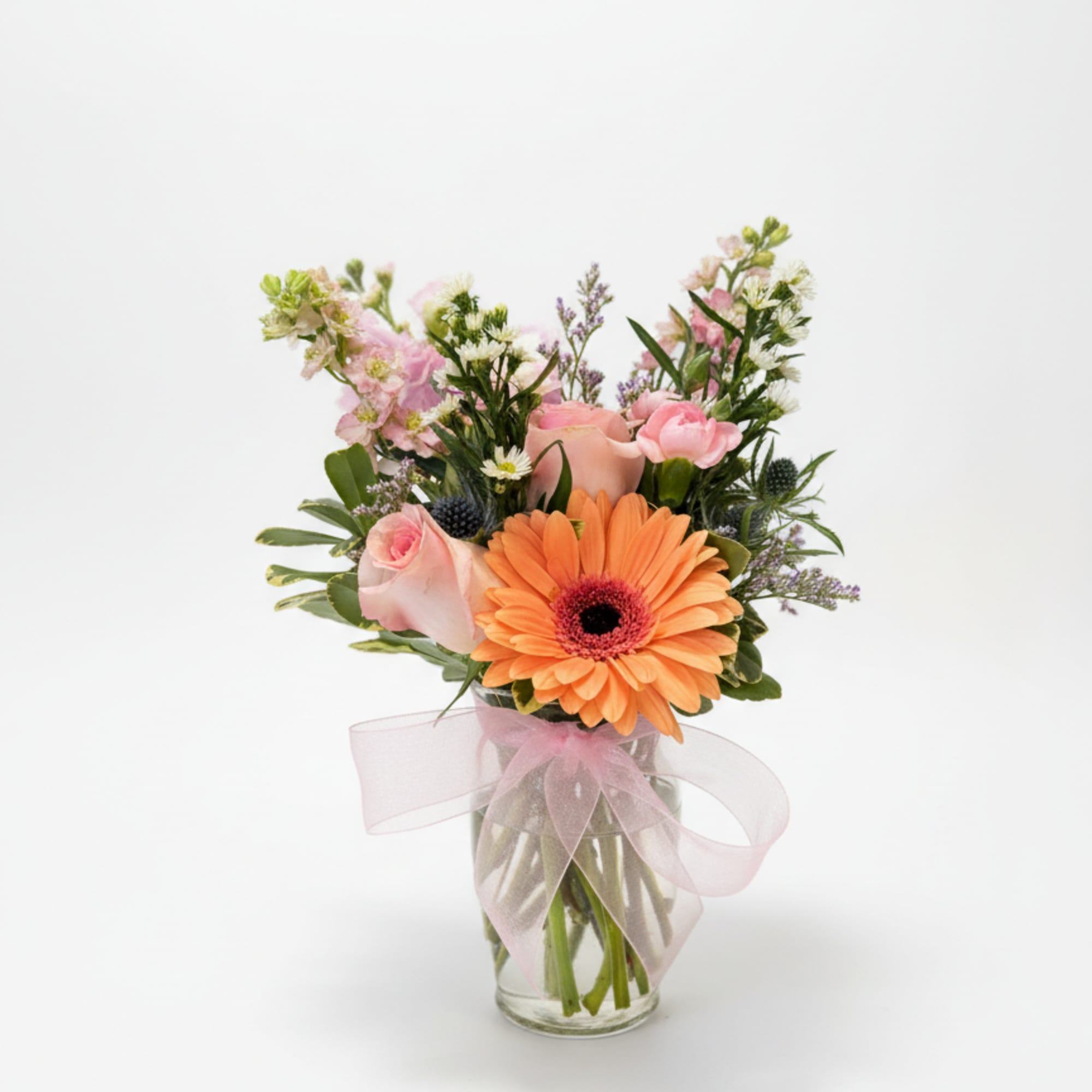 Pink and orange flowers arranged in a glass vase with a pink ribbon