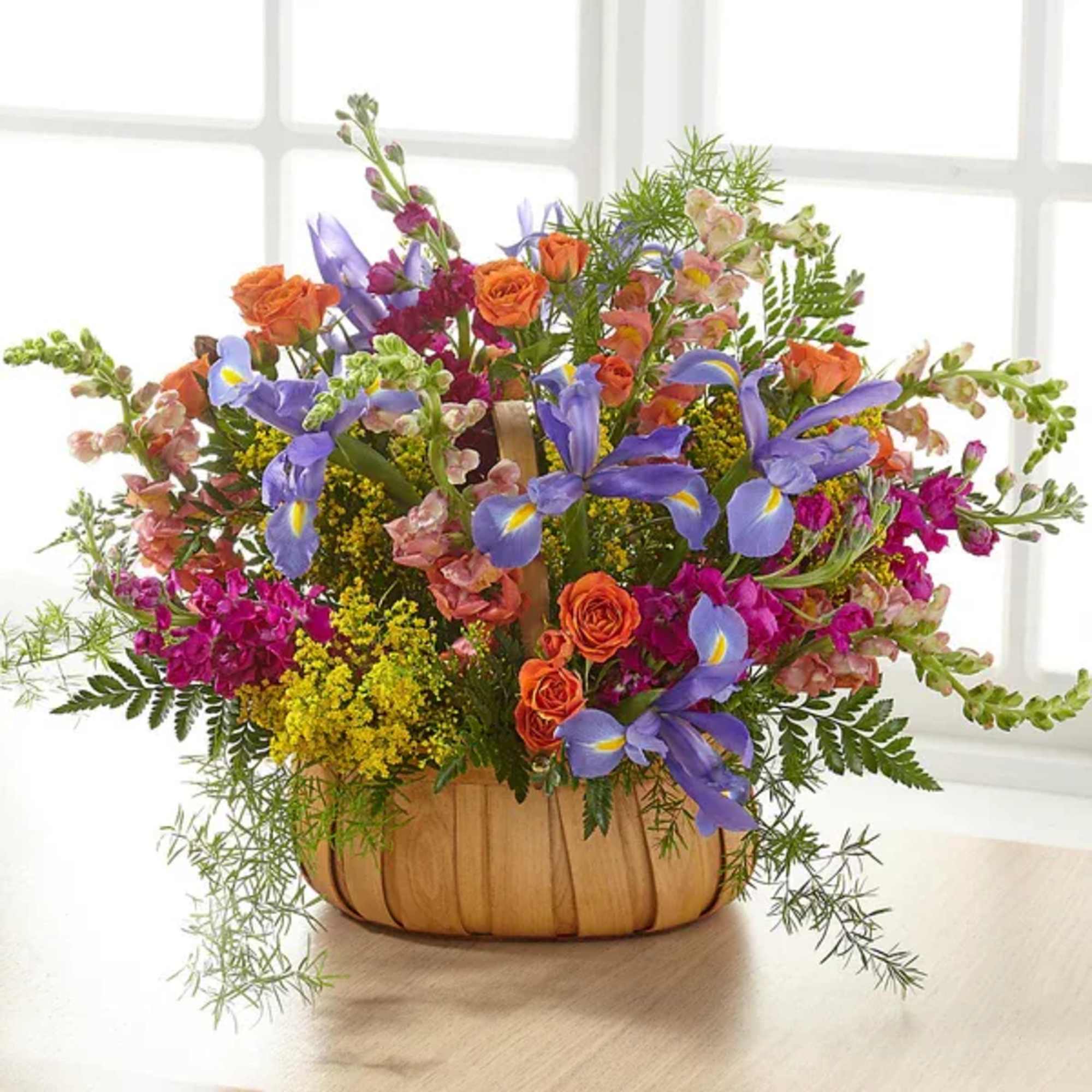 Colorful arrangement of blue irises, orange roses, and mixed blooms in a wooden basket