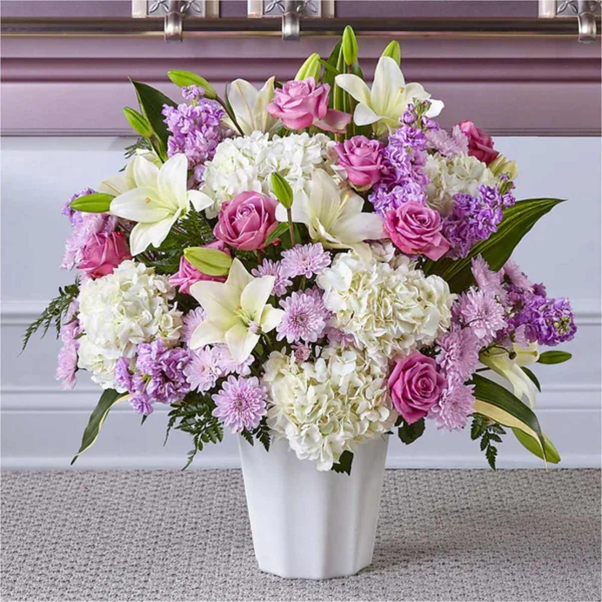 Tall pastel arrangement of white lilies, hydrangeas, and pink roses in a white vase