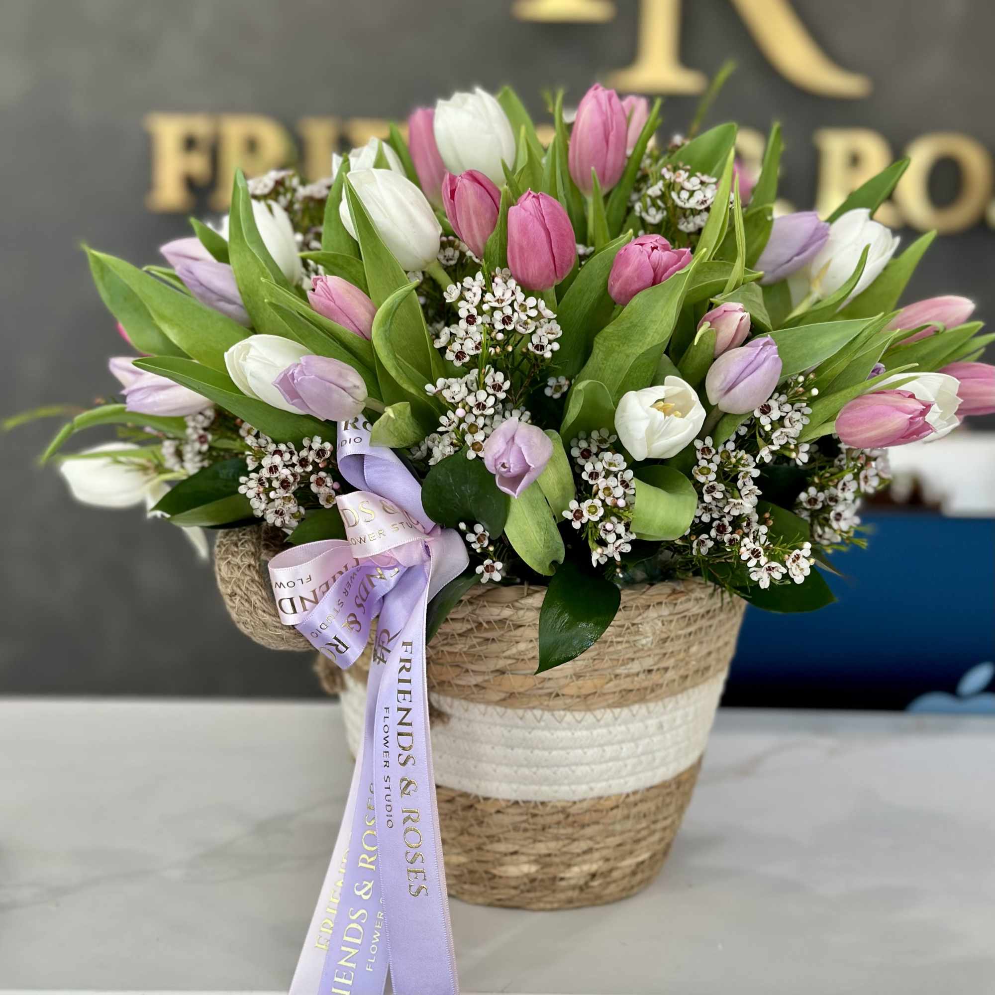 This charming arrangement features fresh tulips artfully nestled in a rustic woven
