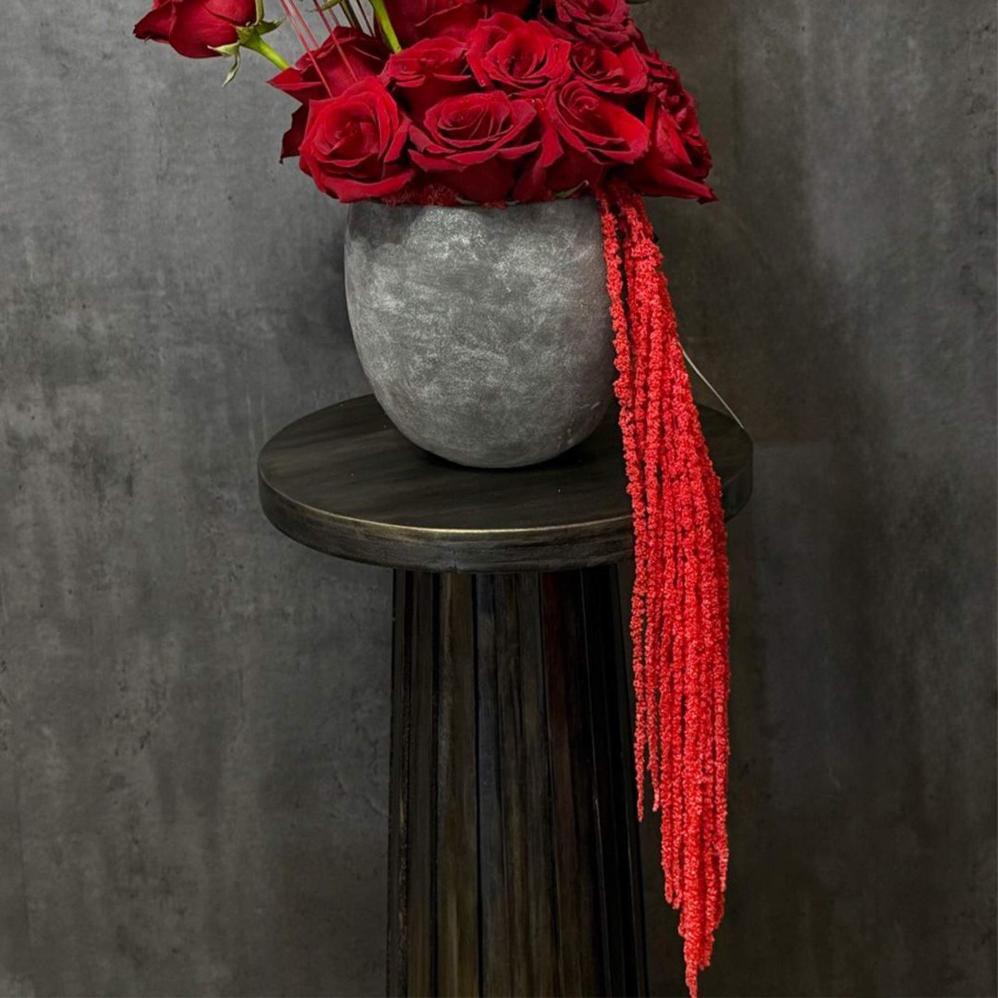 Red roses in a gray vase with a long red hanging accent