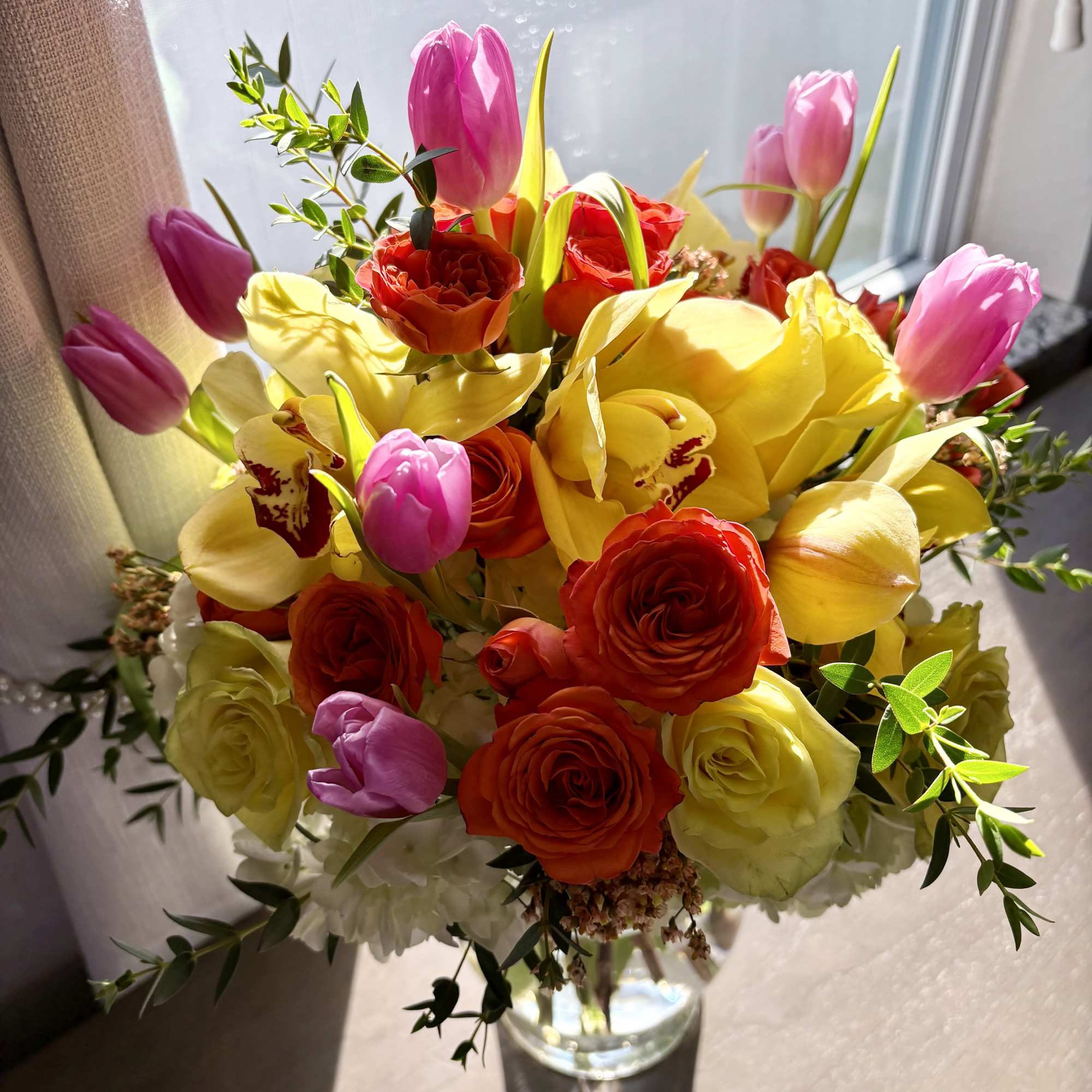 Bouquet of pink tulips, yellow orchids, and red roses in a glass vase