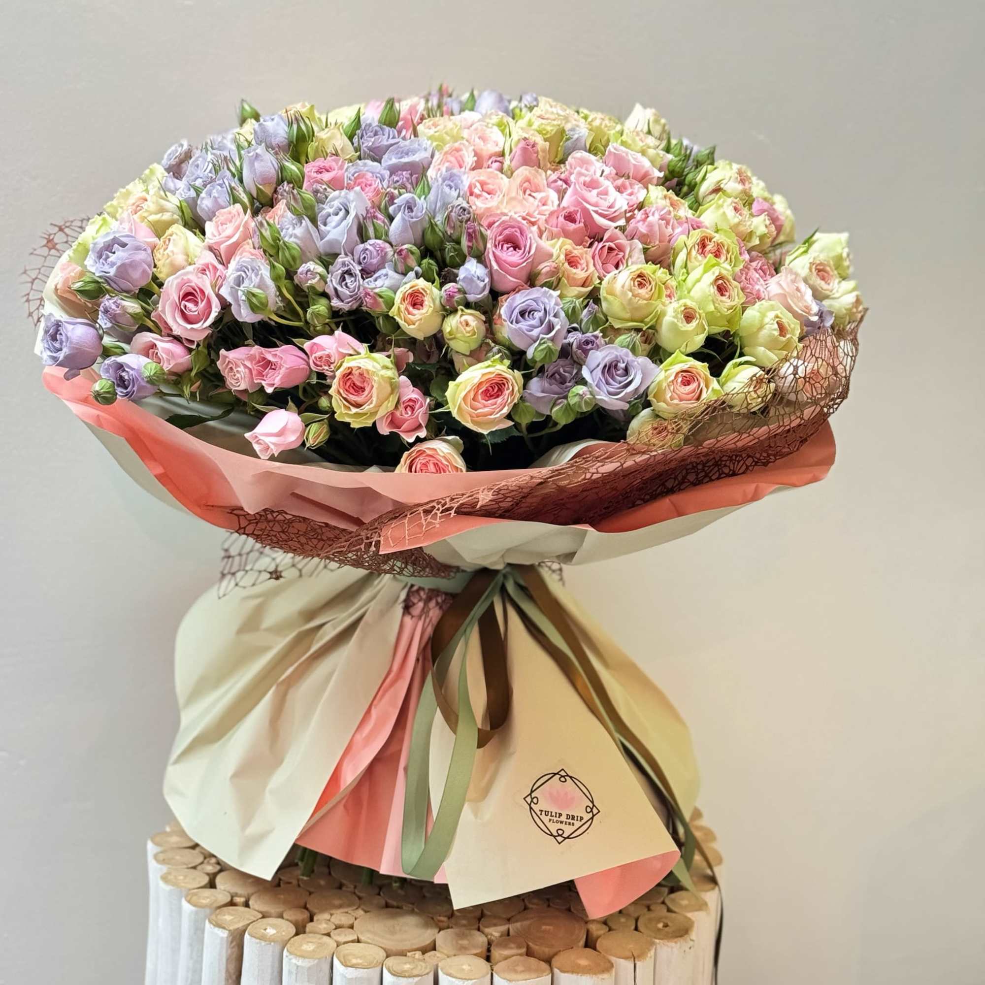 Large bouquet of pastel pink and lavender roses wrapped in cream and pink paper