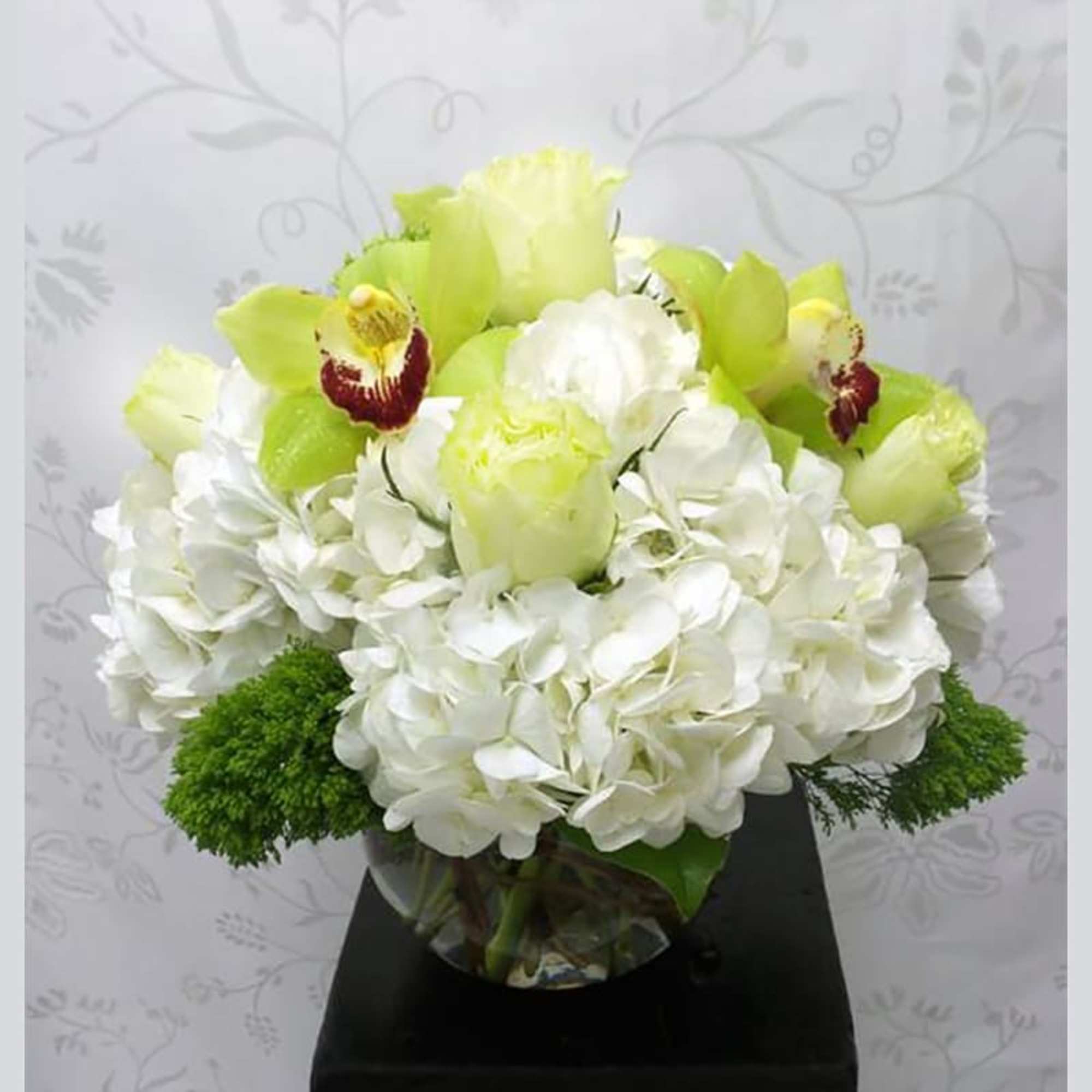 White hydrangeas, lime color roses, and cymbidium orchids arranged in a glass