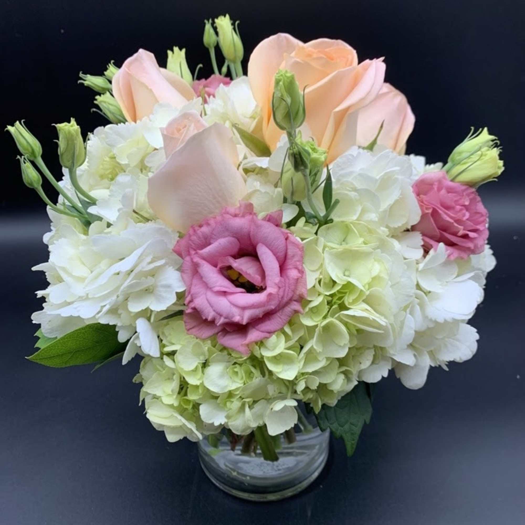 Delicate low and lush arrangement of white hydrangea, peach roses and pink