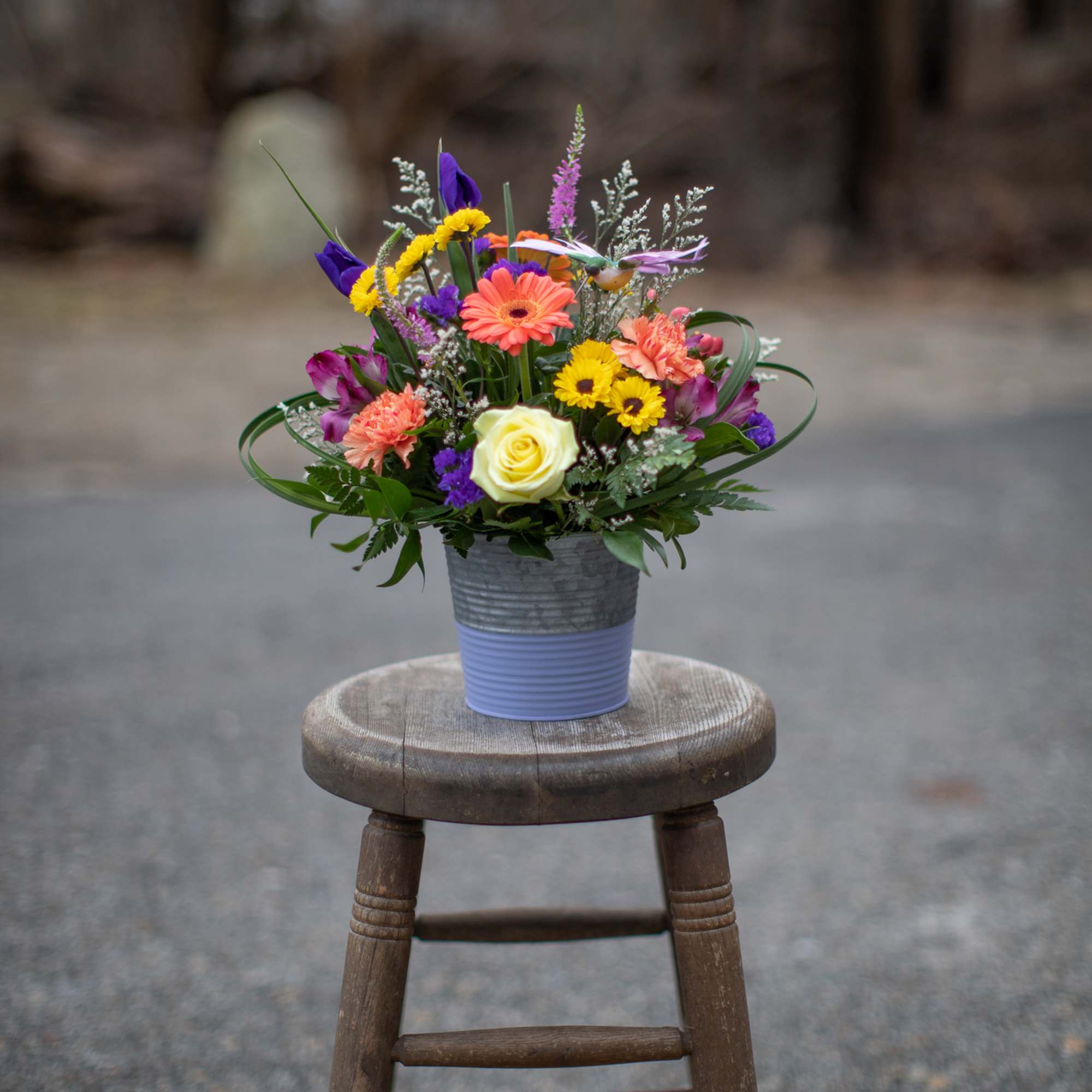 Colorful mixed flower arrangement in a small metal pot on a wooden stool