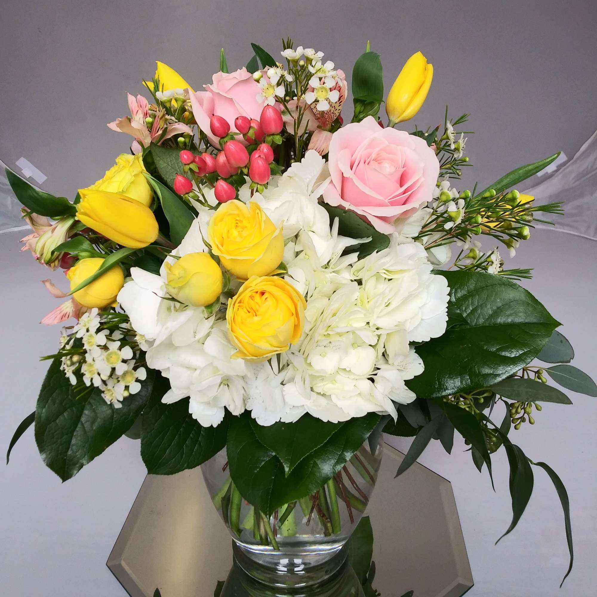 Bouquet of pink and yellow roses with white hydrangeas in a glass vase