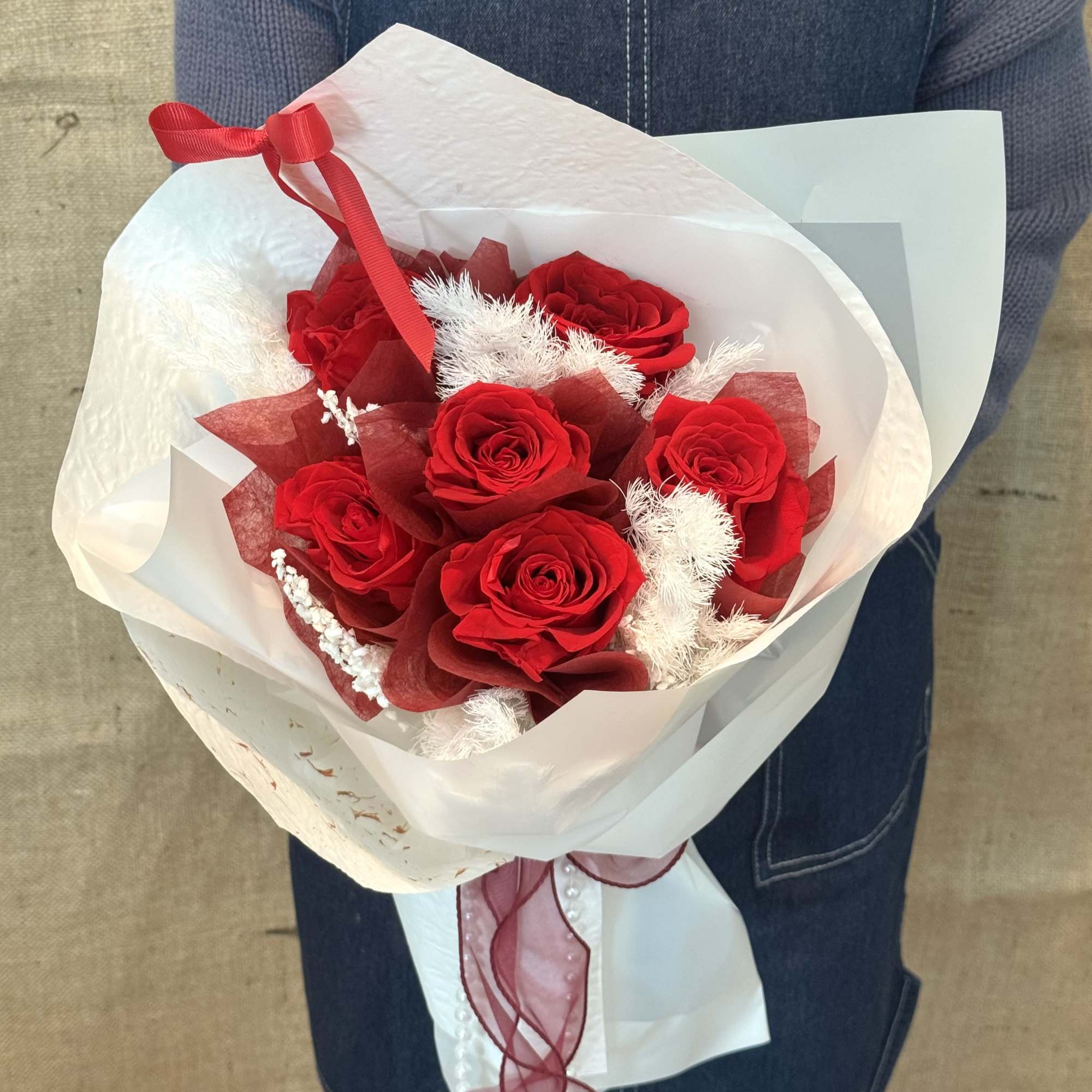 This shows a bouquet of bright red roses wrapped in white wrapping