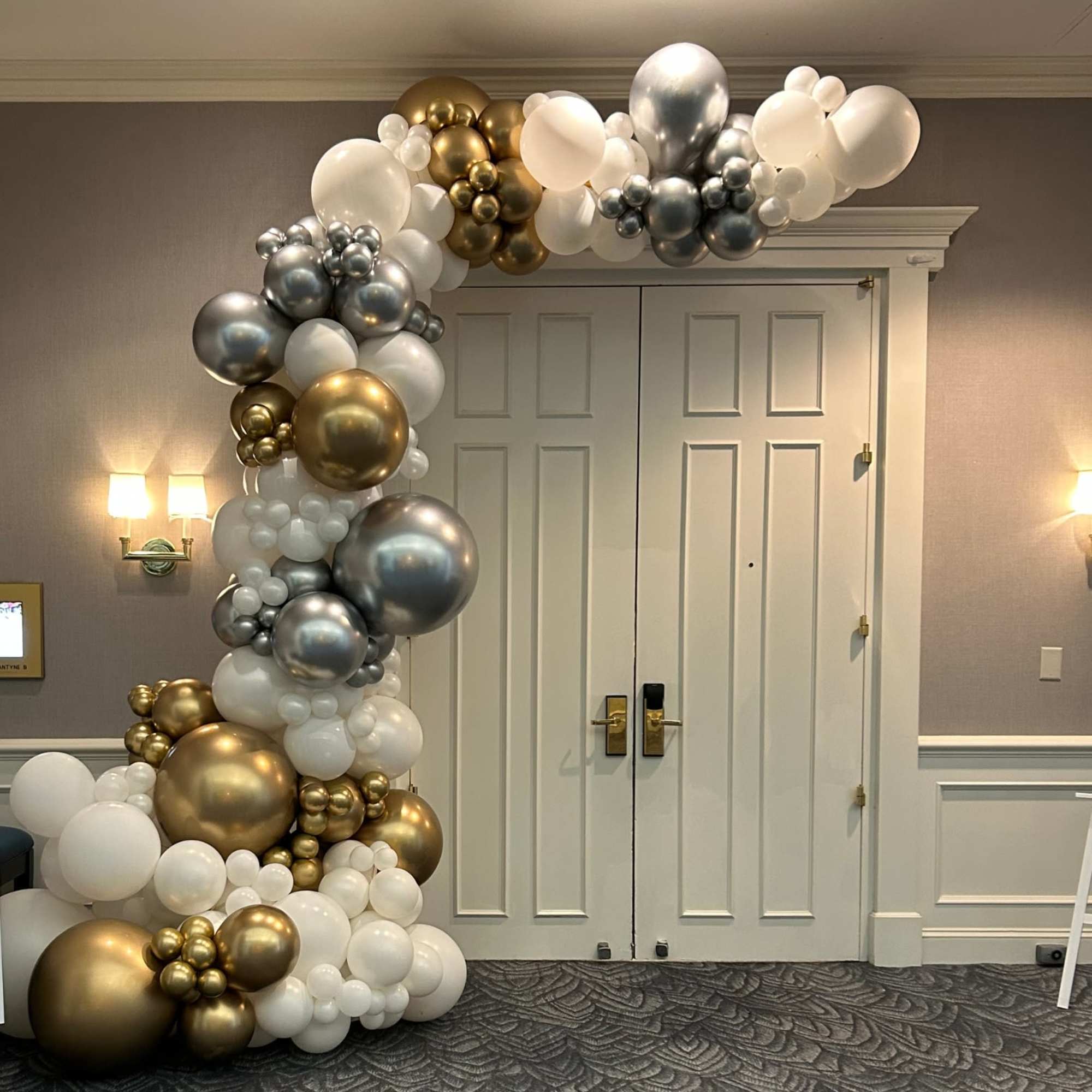 Balloon arch in white, gold, and silver around double doors