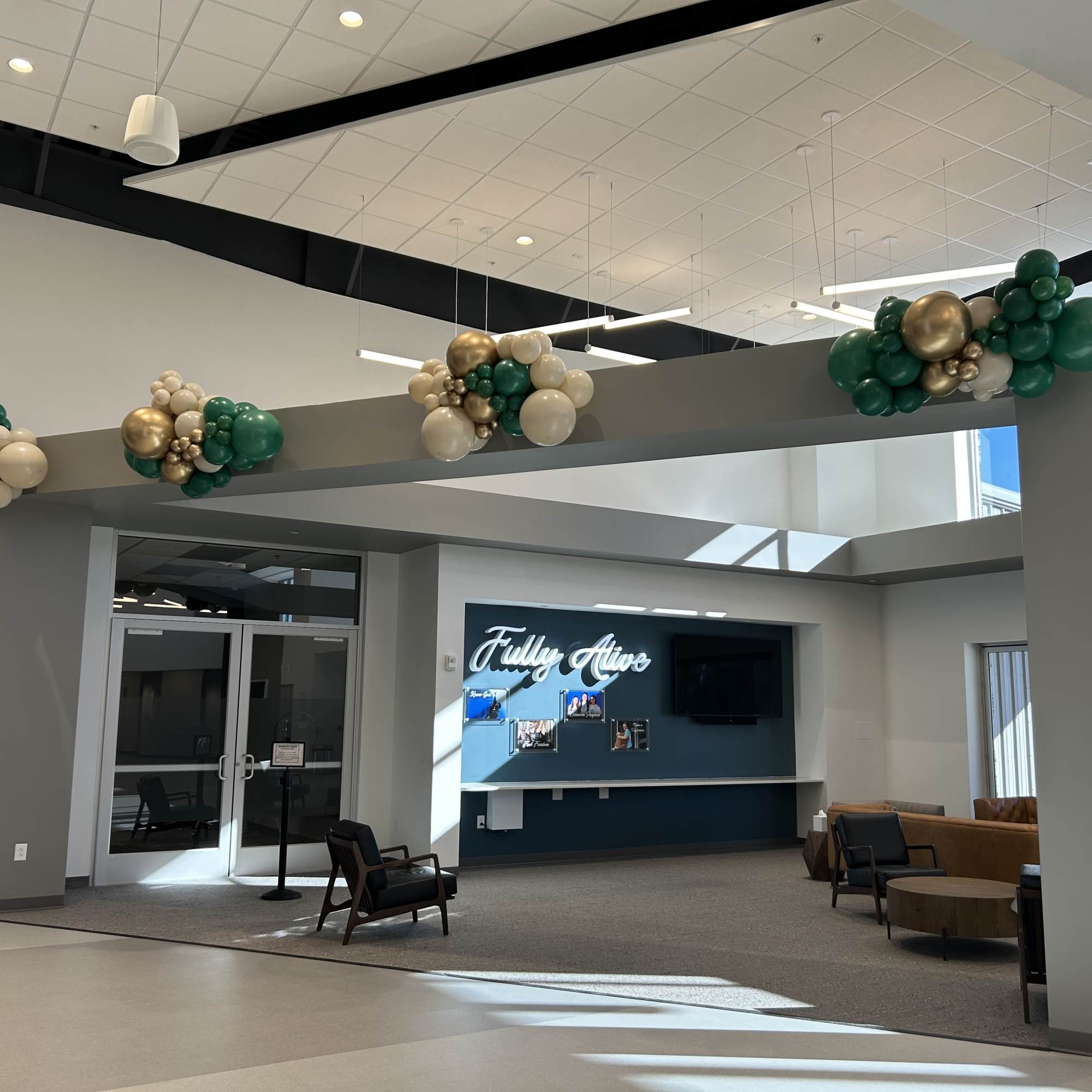 Balloon clusters in green, white, and gold hang from a lobby beam.