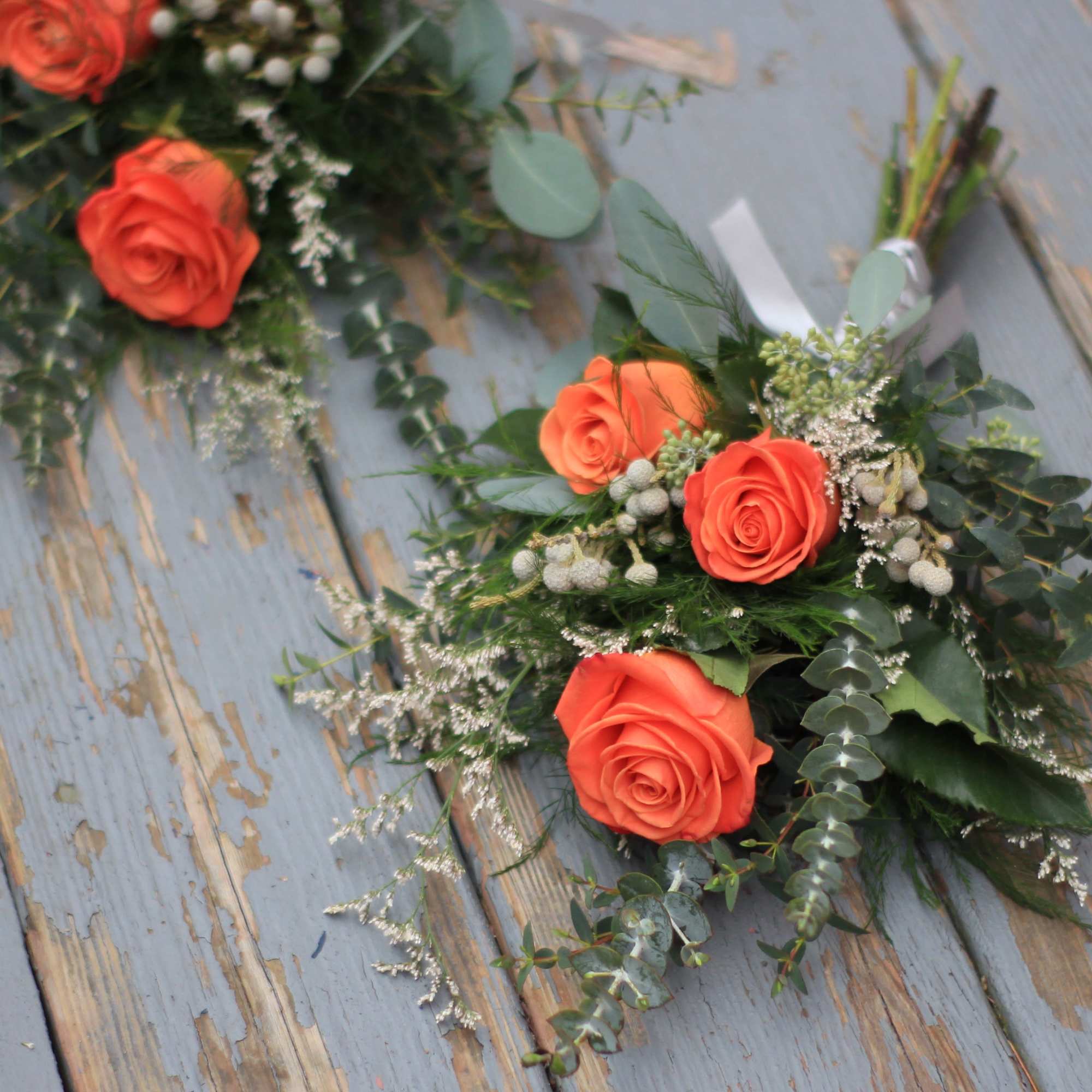 Orange rose bouquets with greenery on a weathered wooden surface