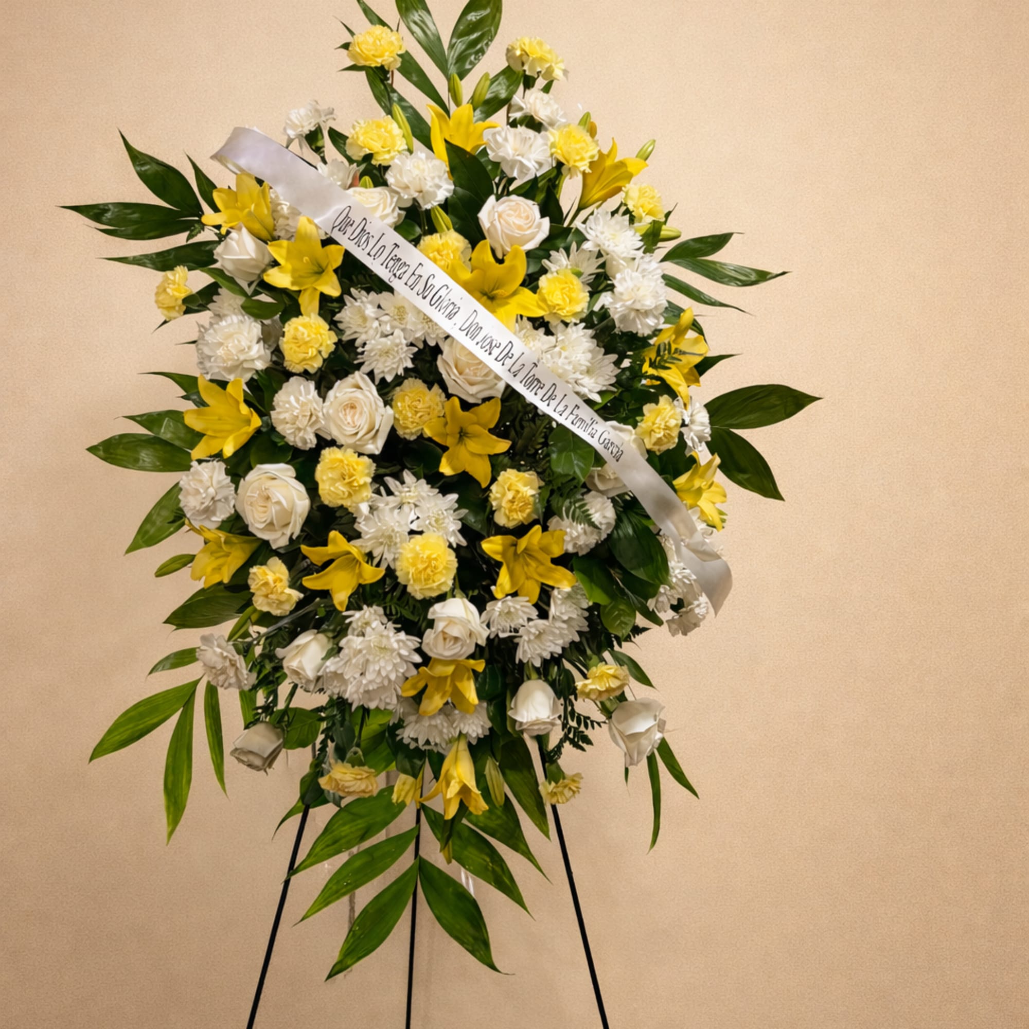 A radiant sympathy tribute featuring yellow lilies, white roses, and soft carnations