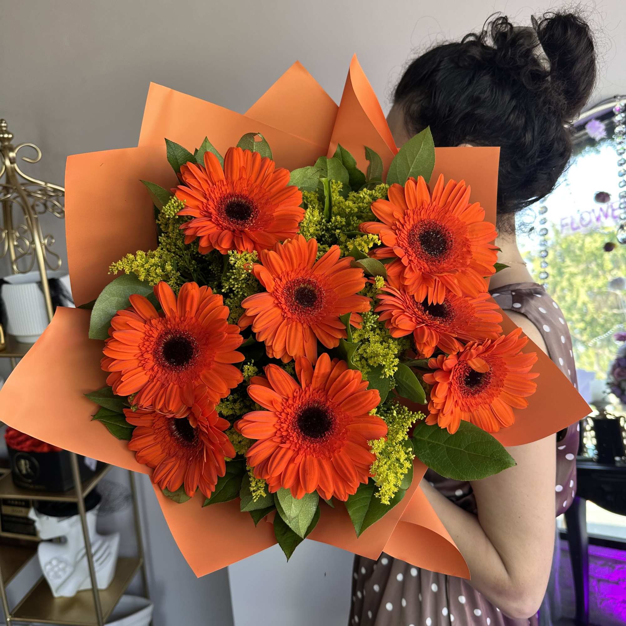 A vibrant bouquet of bright orange gerbera daisies, wrapped in matching tones