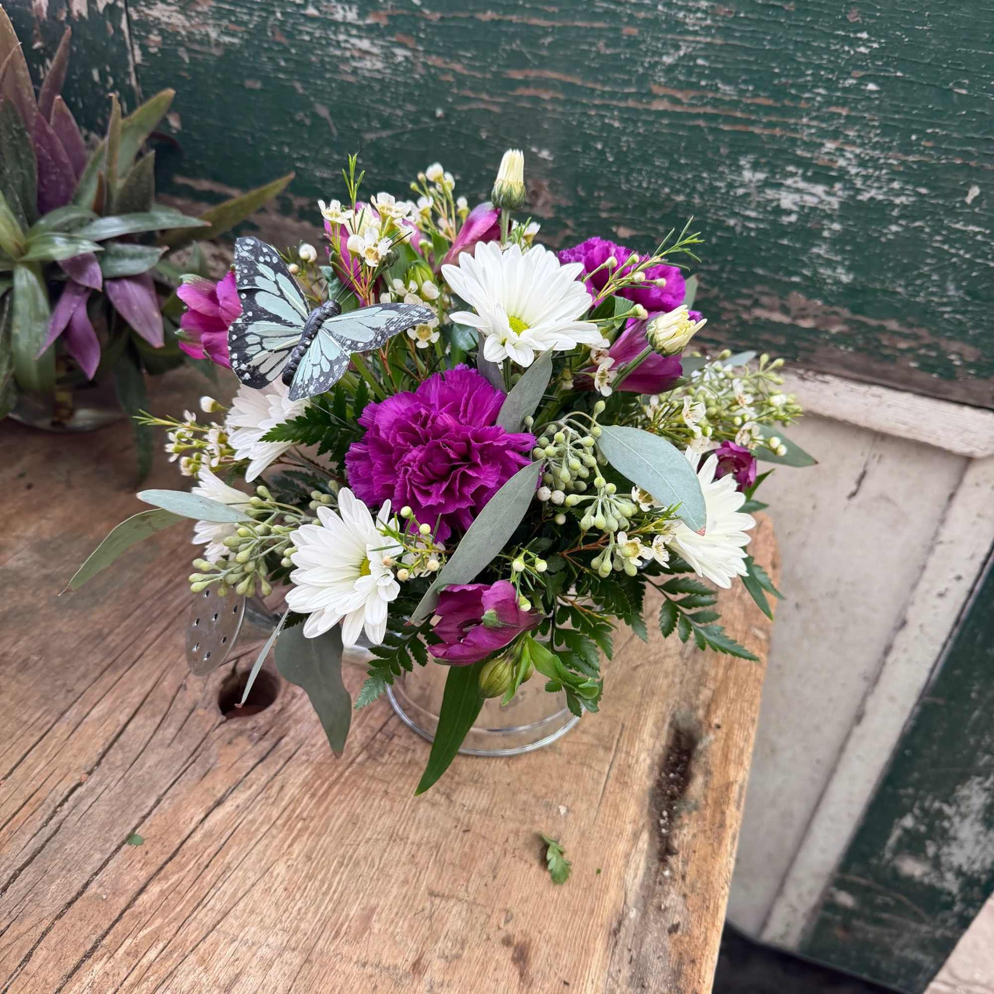 Bouquet of white daisies and purple flowers in a clear vase with a butterfly decoration