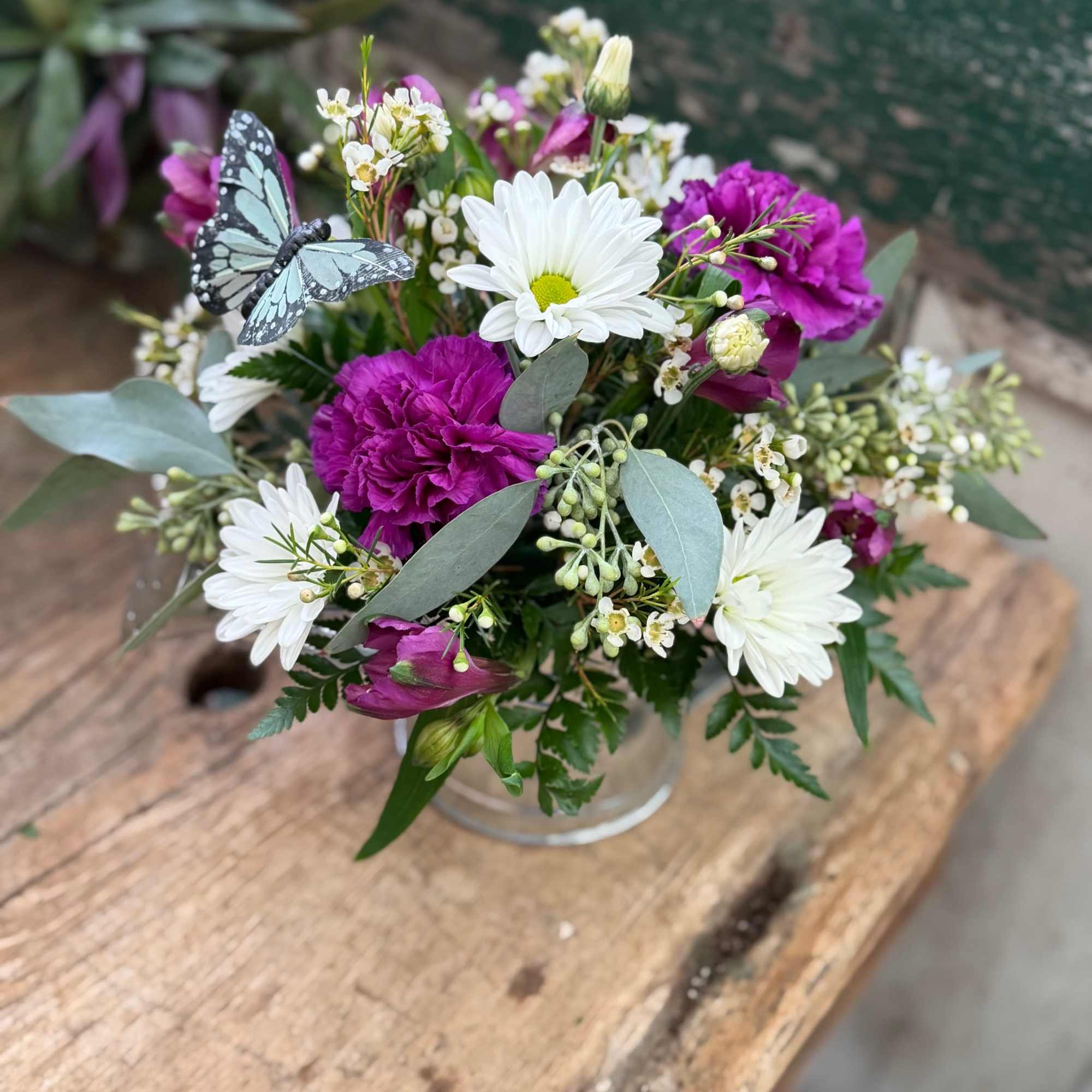 Bouquet of white daisies and purple carnations in a glass vase with a butterfly decoration
