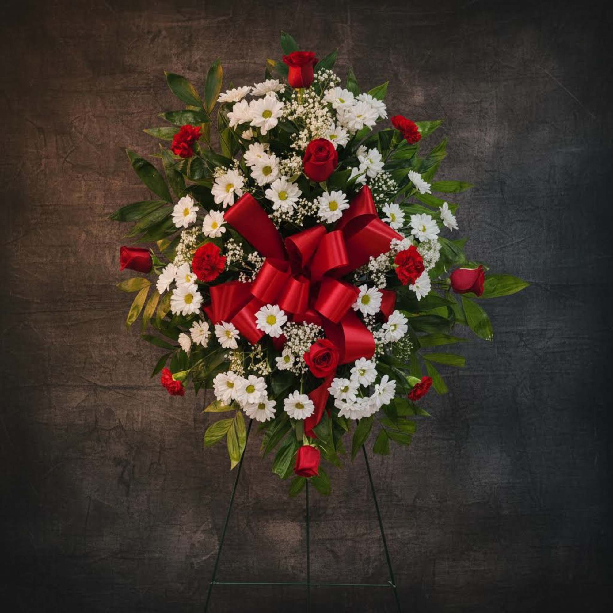 Standing floral wreath with red roses, white daisies, and a red ribbon bow