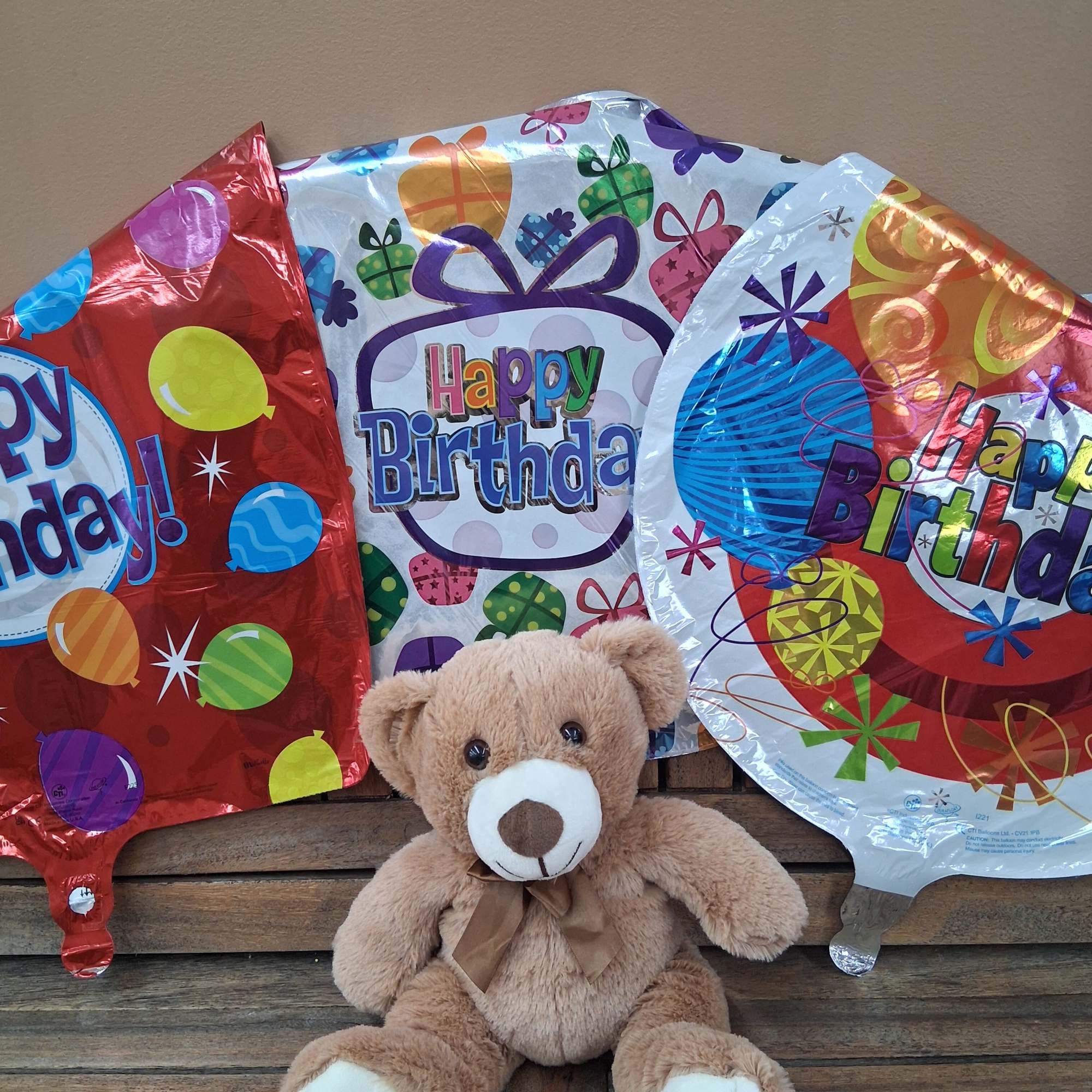 Teddy bear with three birthday balloons