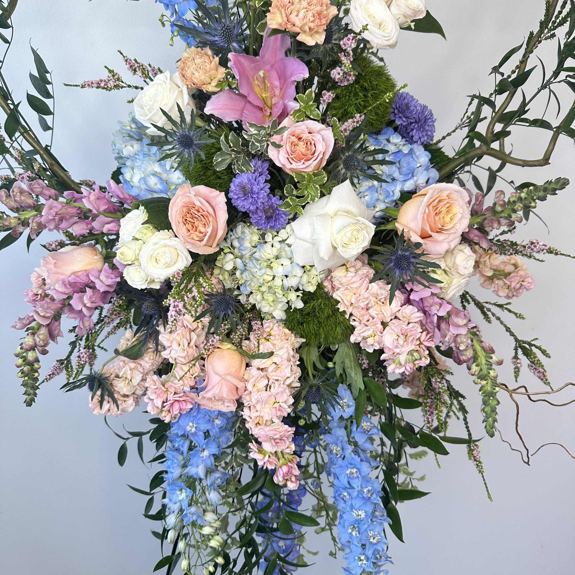 Large pastel floral spray with roses, lilies, and blue delphinium on a stand