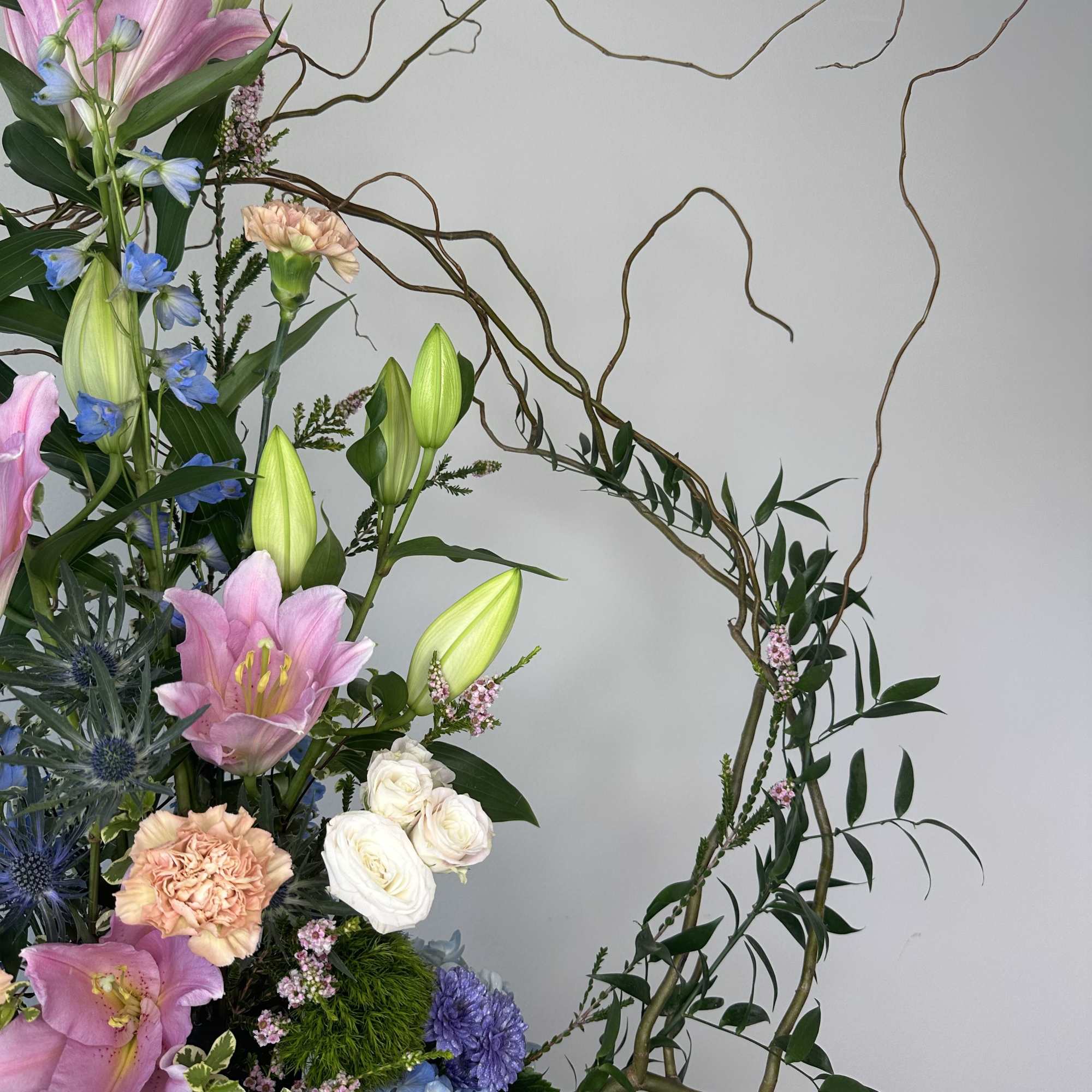 Tall floral arrangement with pink lilies, roses, and blue blooms on twisting branches