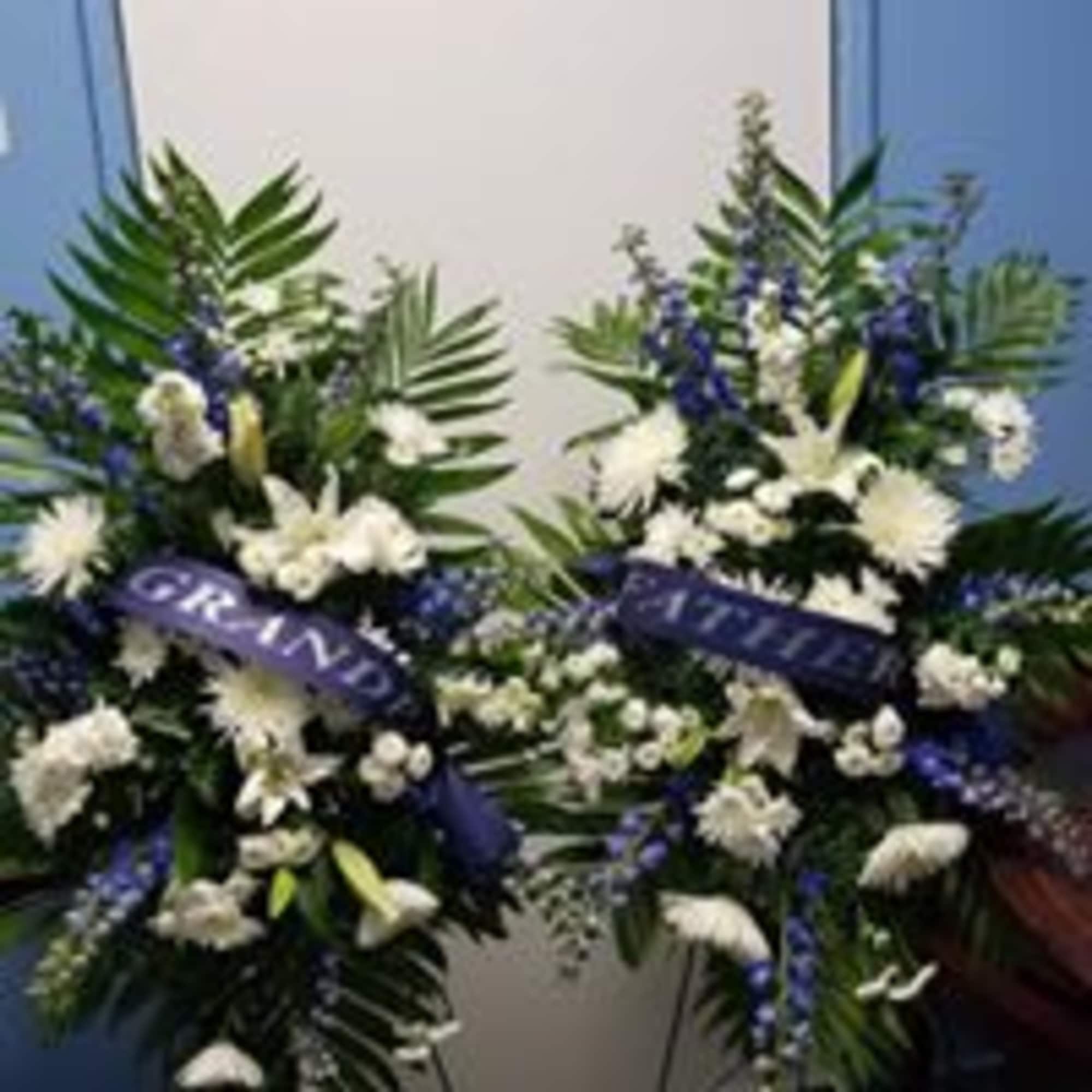 Two blue-and-white funeral wreaths with ribbon banners