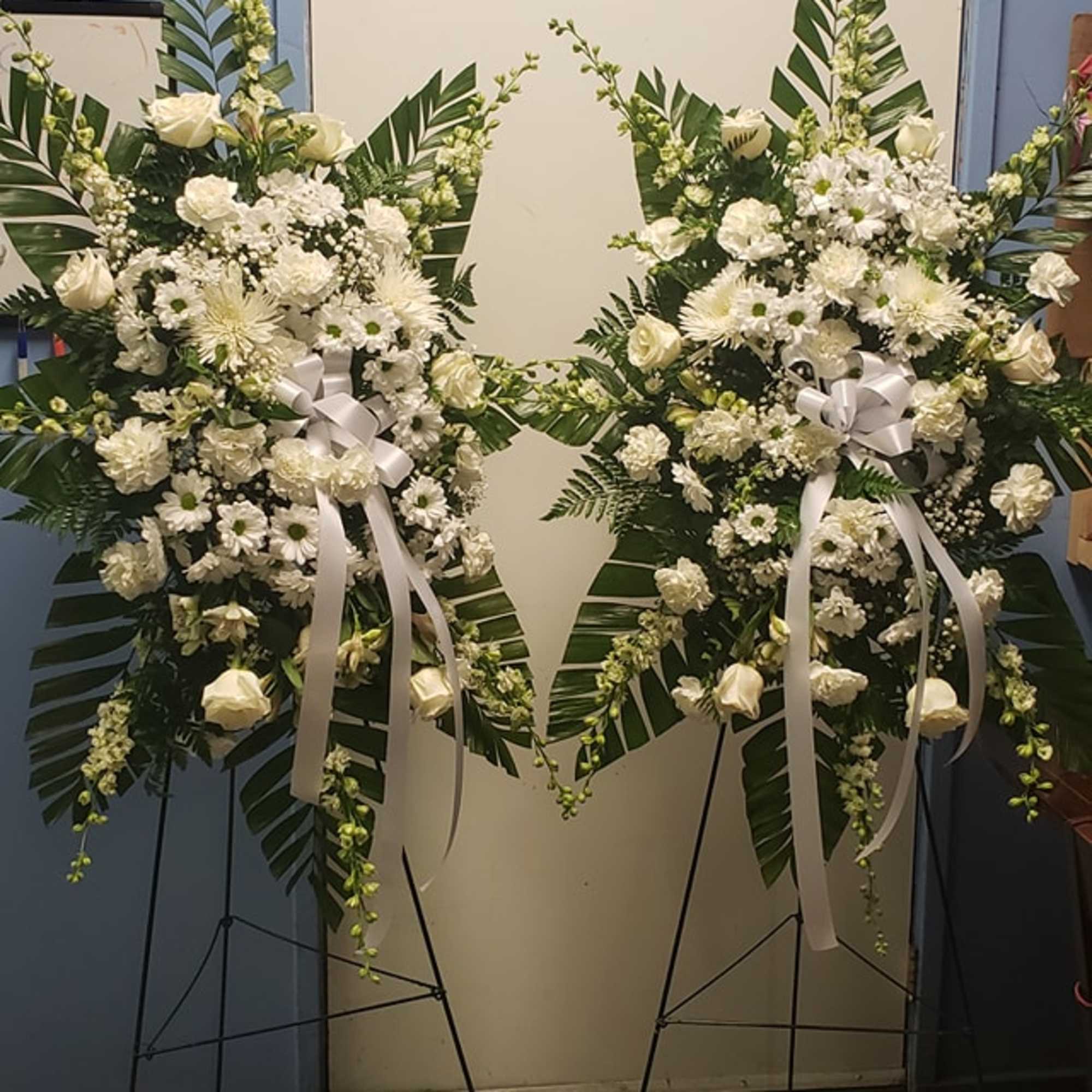 Two white floral standing sprays on easels with ribbon bows