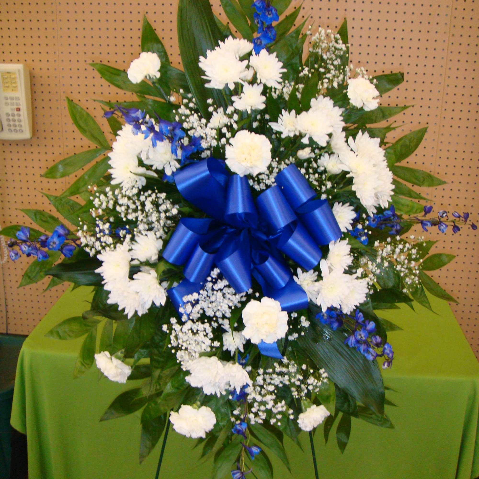 Large standing floral spray with white blooms, blue accents, and a blue ribbon