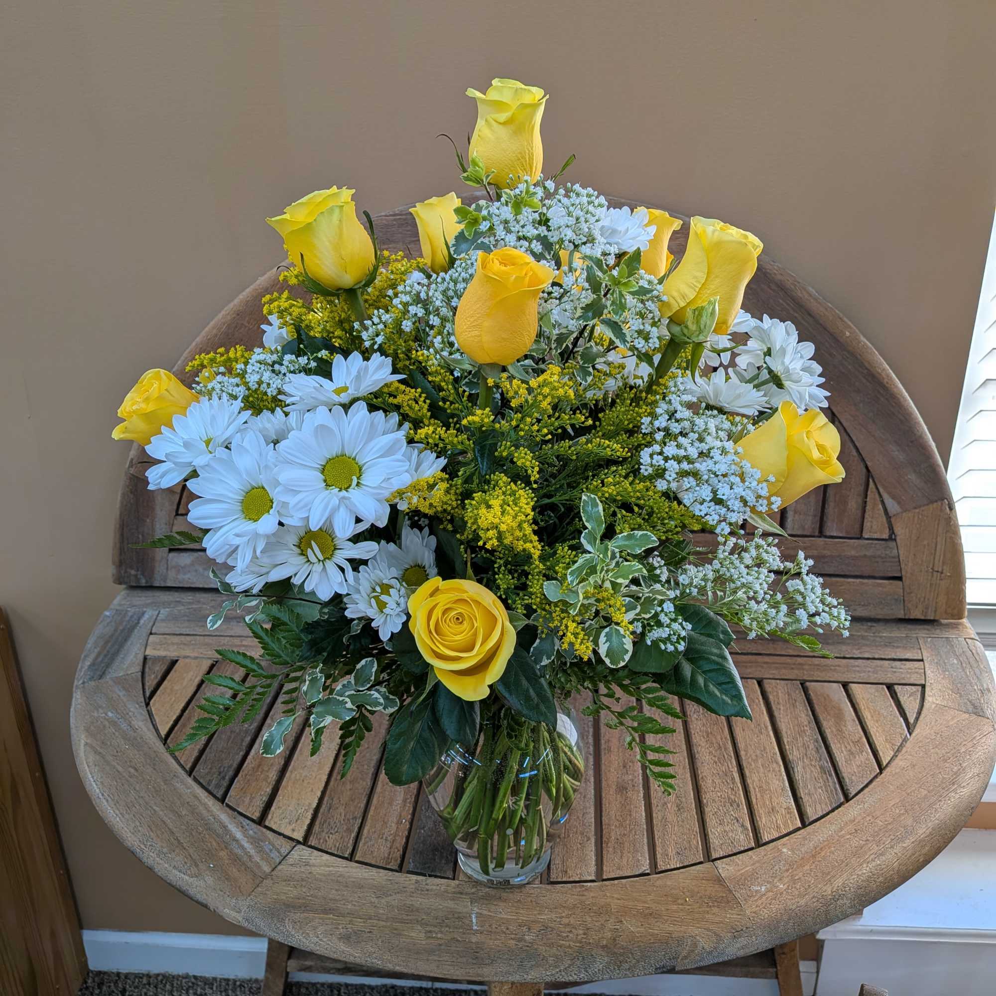Yellow roses and white daisies arranged in a glass vase