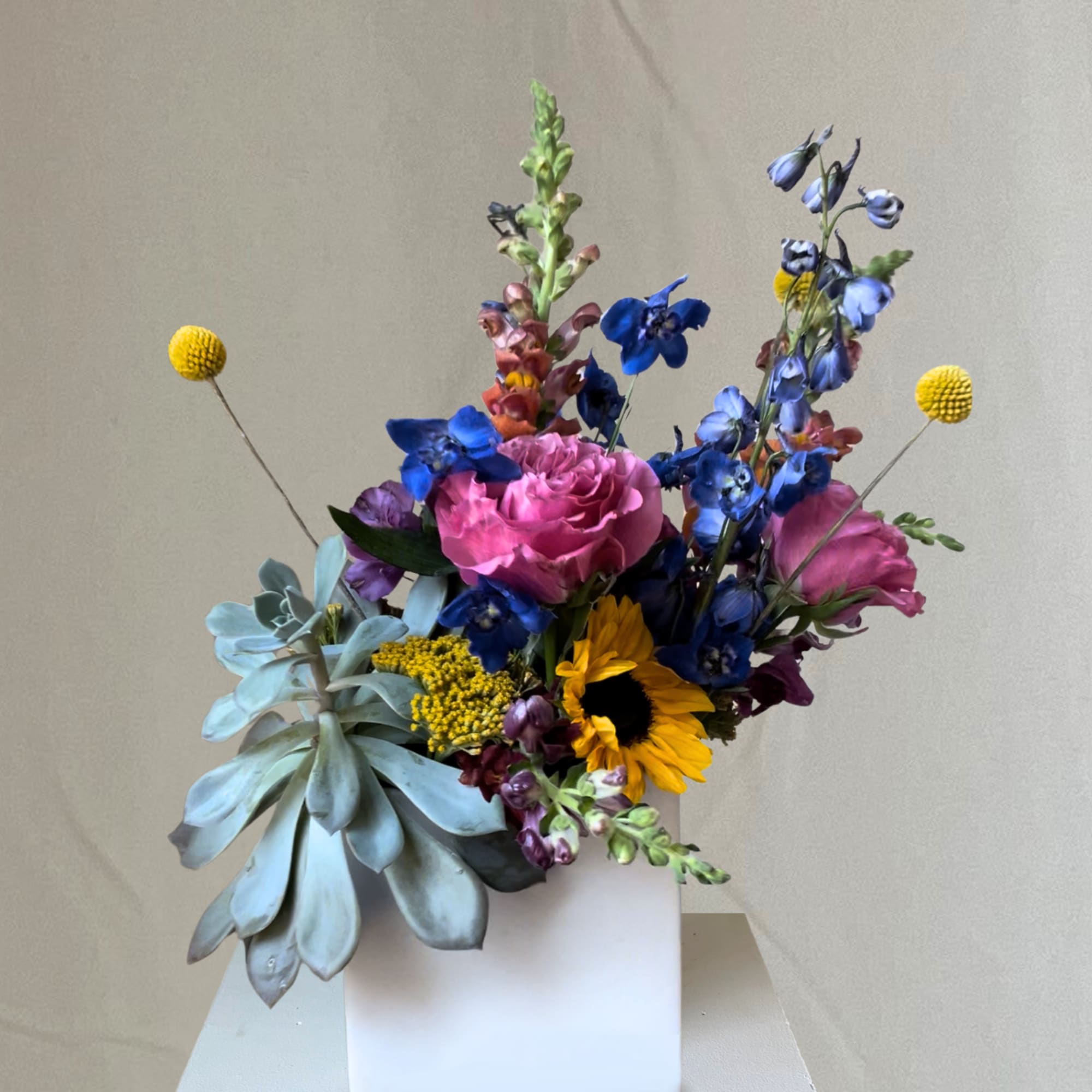 Colorful bouquet in a white square vase with pink roses and blue flowers