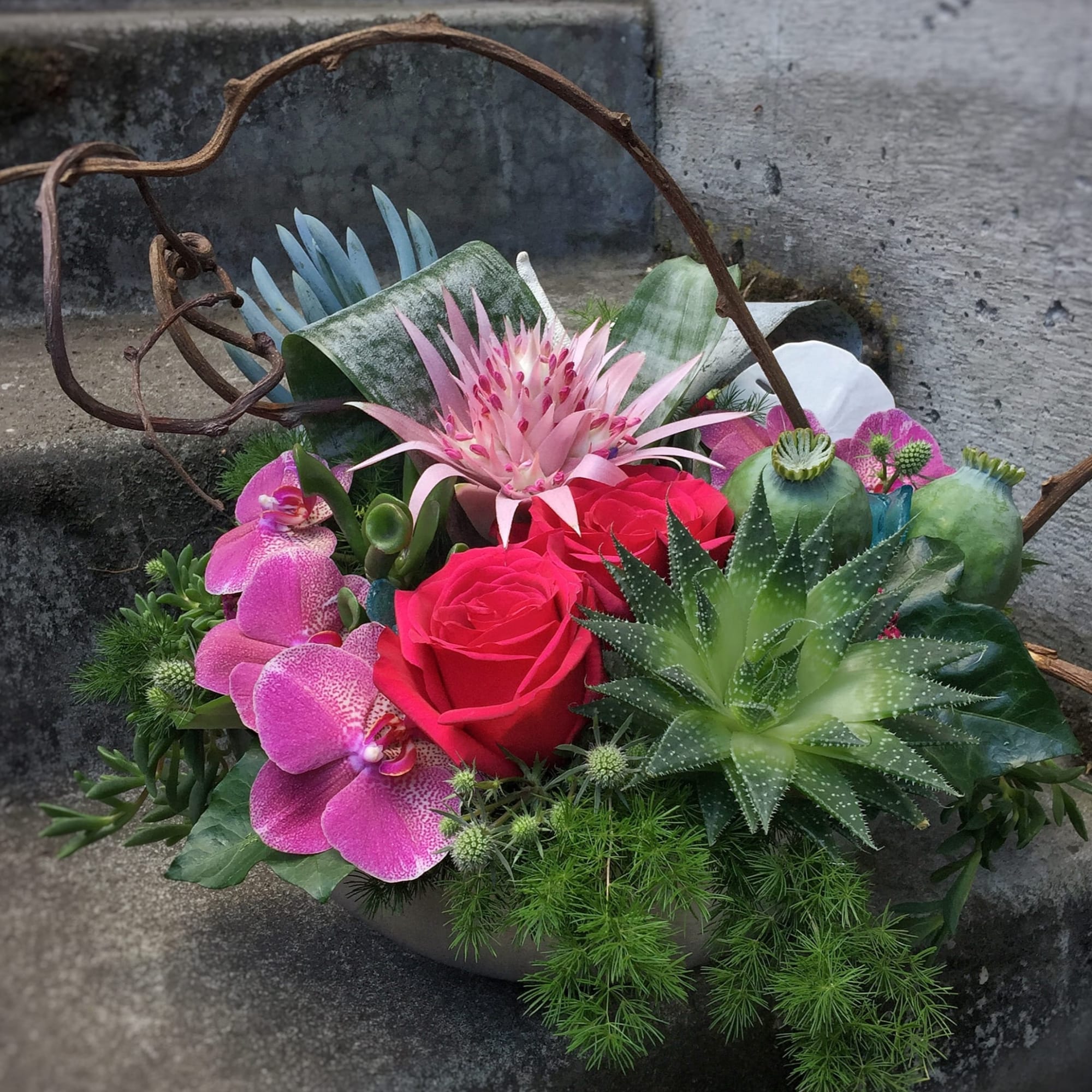 Mixed floral arrangement with pink roses, orchids, and succulents in a basket