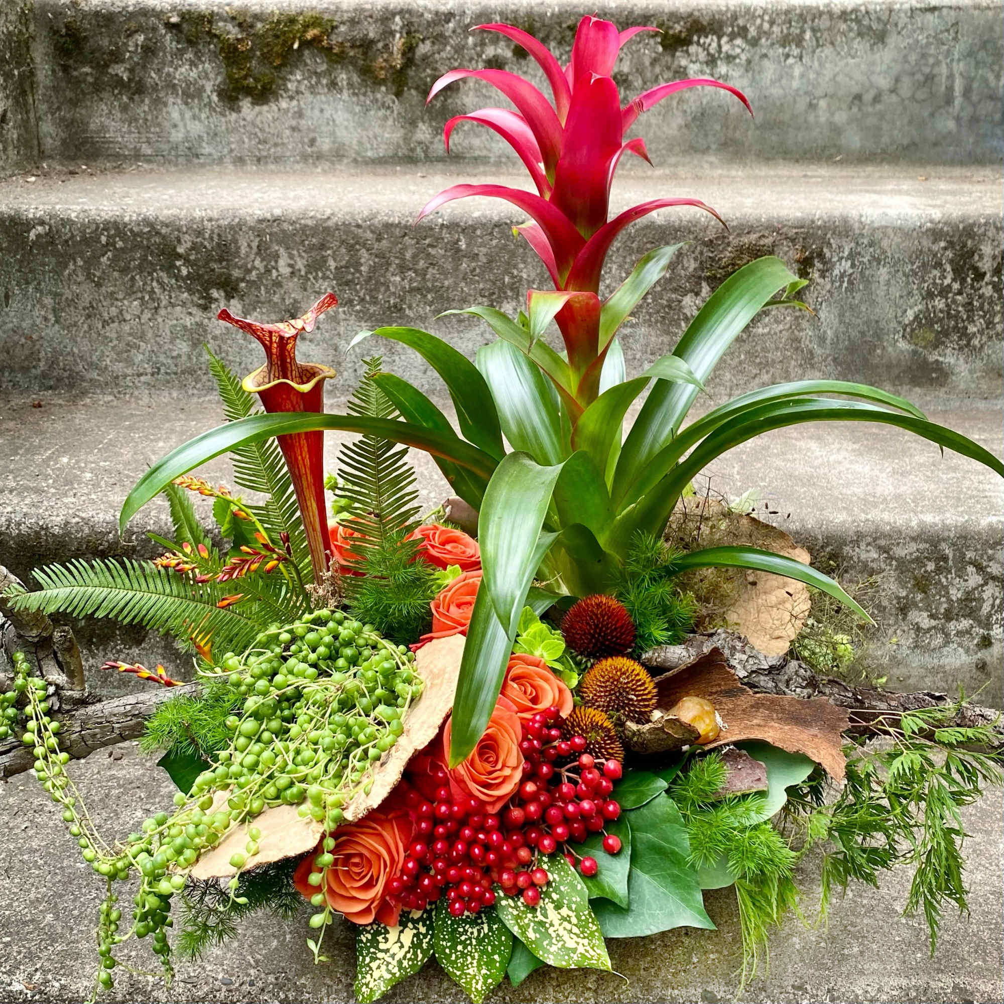 Tropical floral arrangement with pink bromeliad, orange roses, and red berries